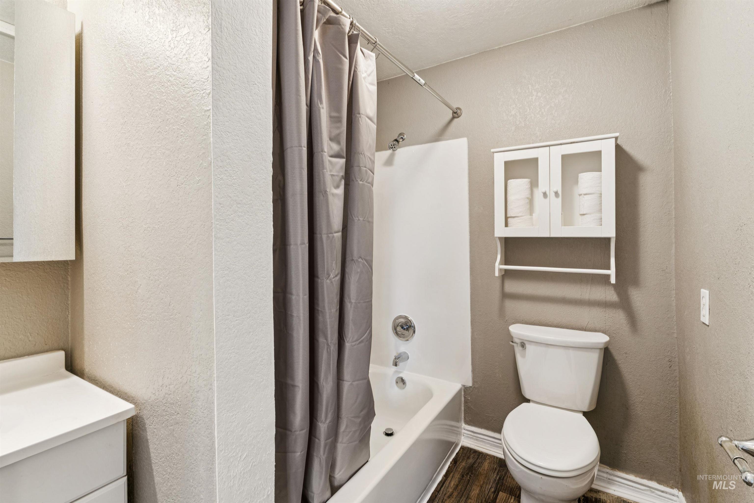 Bathroom featuring a textured wall, shower / bath combination with curtain, vanity, and wood finished floors