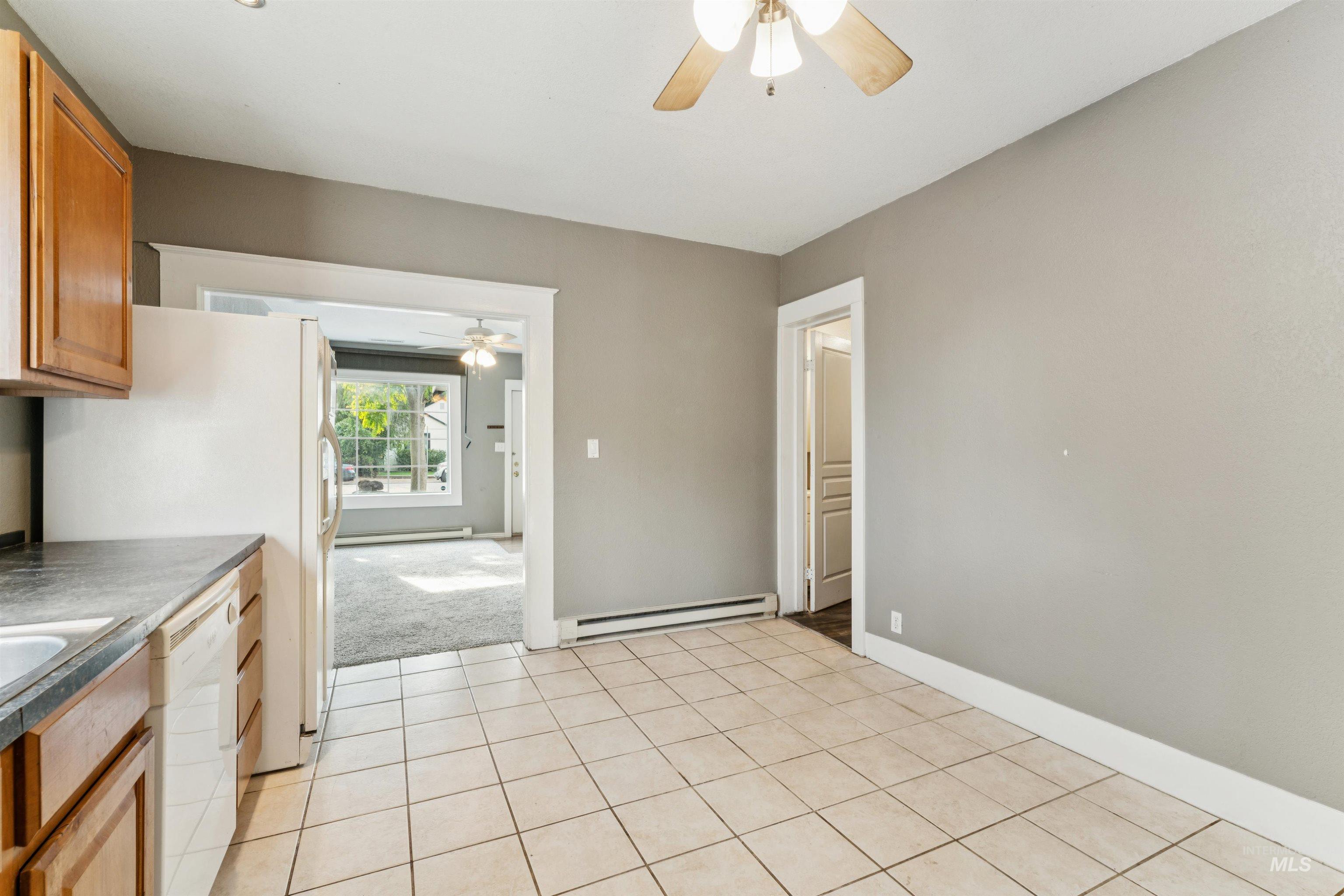 Kitchen featuring a ceiling fan, light tile patterned floors, white appliances, a baseboard radiator, and brown cabinetry