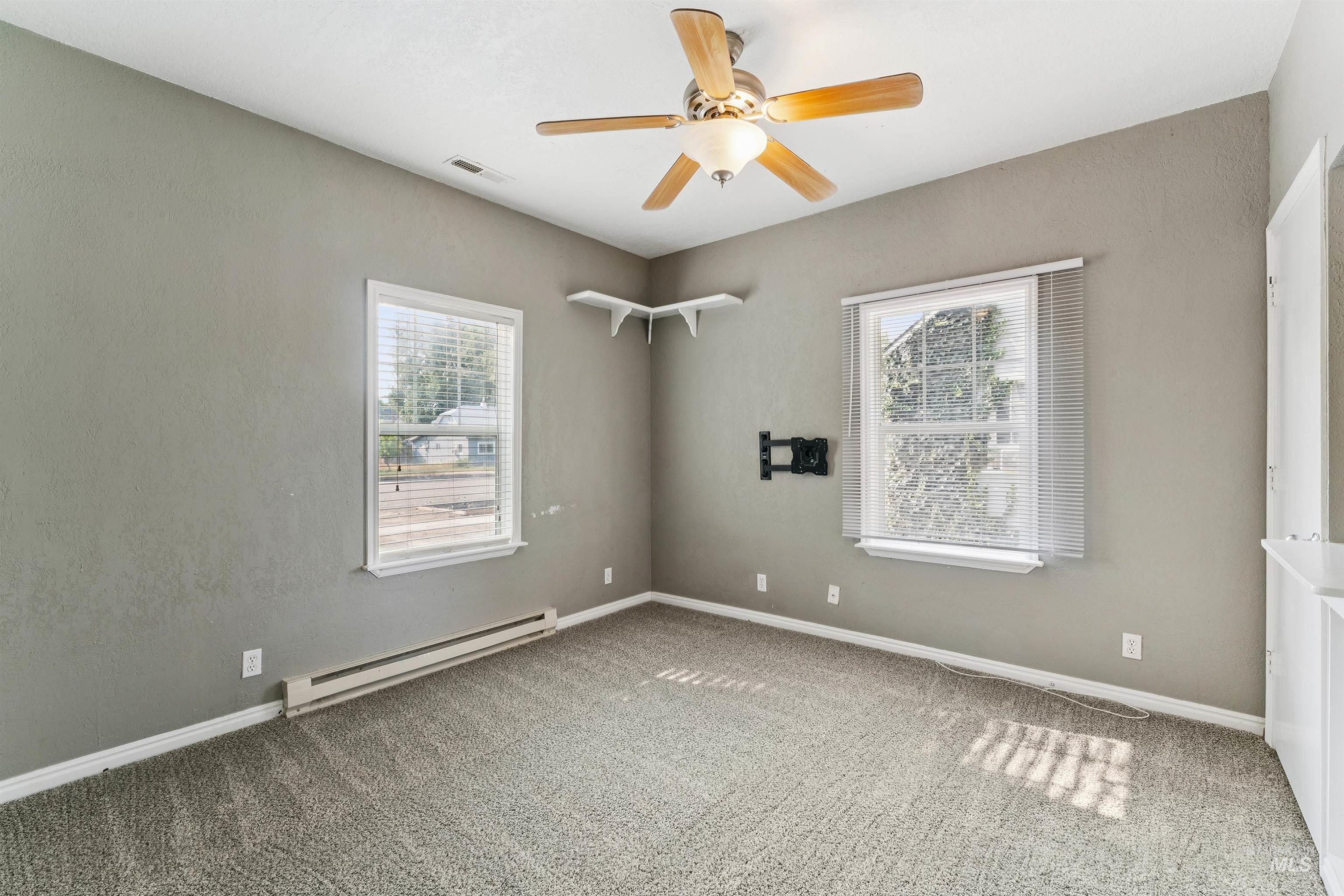 Empty room featuring a baseboard radiator, carpet floors, ceiling fan, and healthy amount of natural light