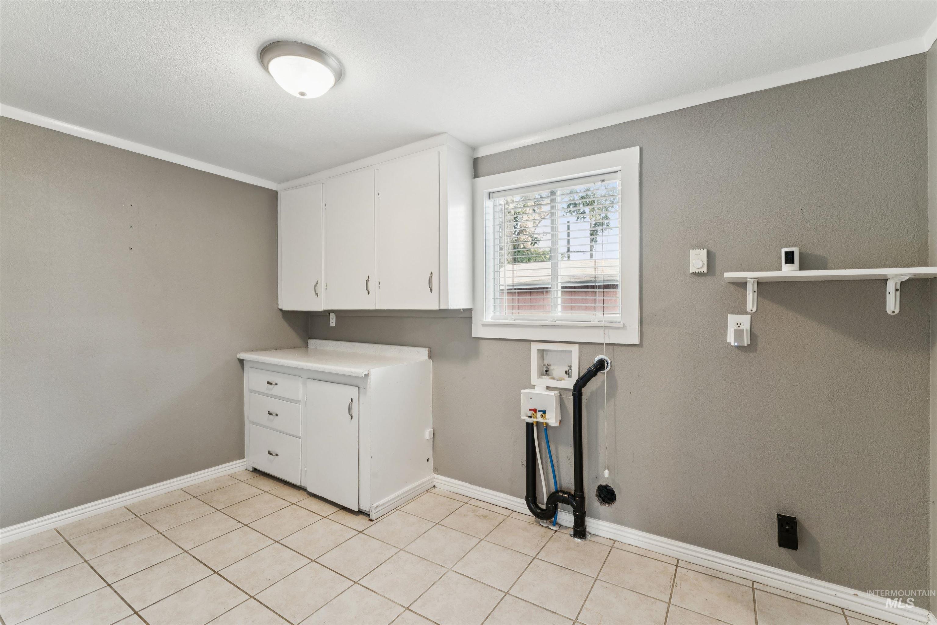 Laundry area featuring cabinet space, washer hookup, light tile patterned floors, and a textured ceiling