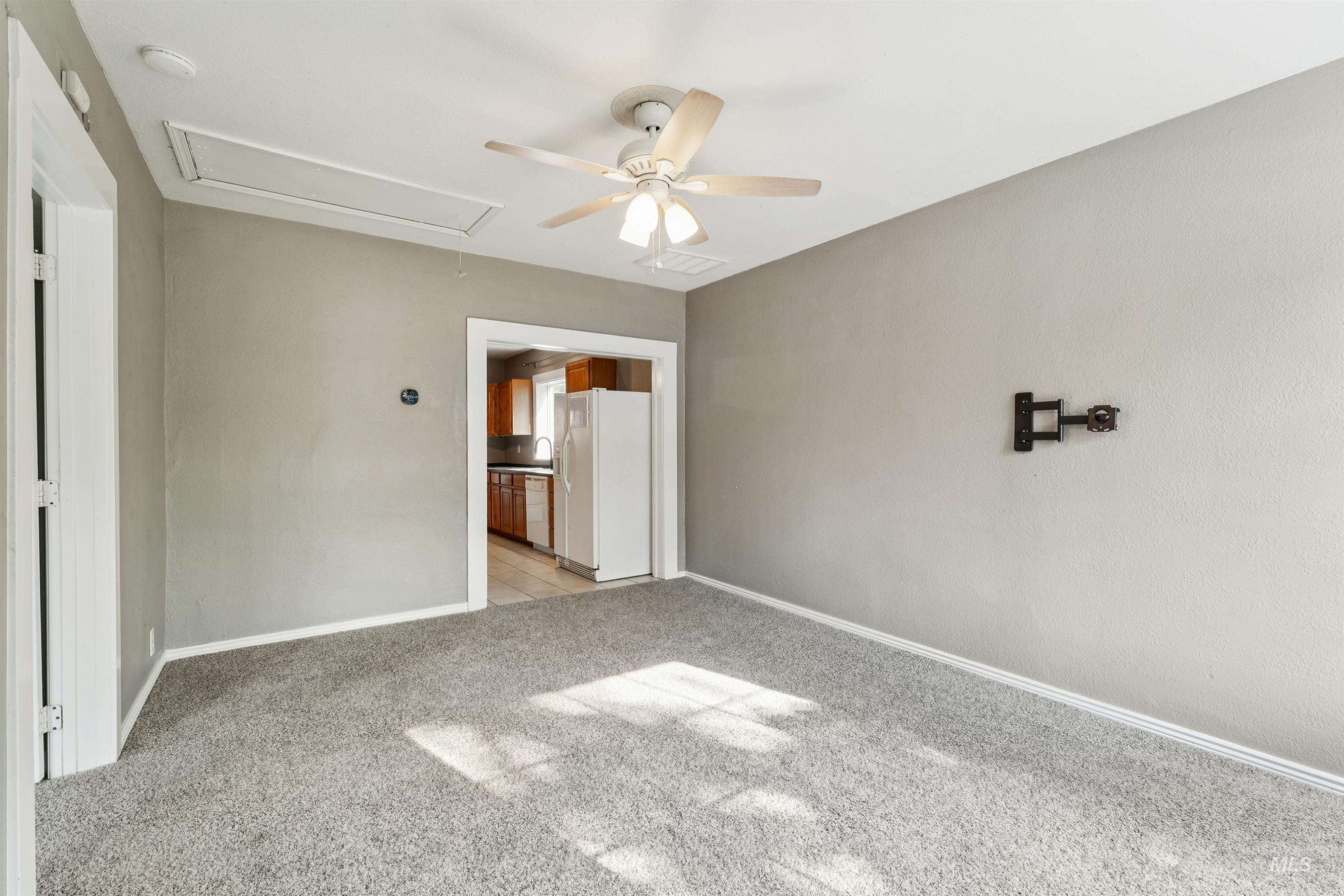 Unfurnished bedroom featuring attic access, white refrigerator with ice dispenser, light colored carpet, and ceiling fan