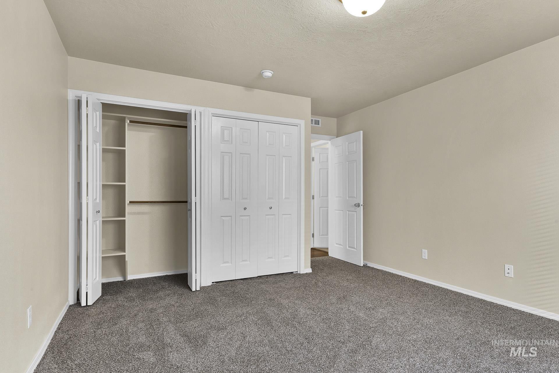 Unfurnished bedroom with carpet floors, a textured ceiling, and multiple closets