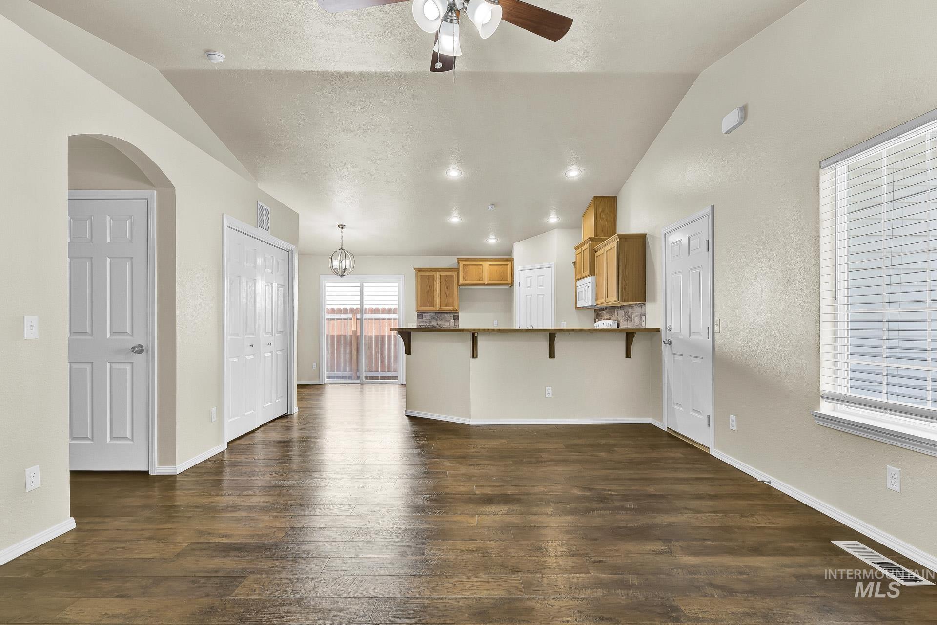 Unfurnished living room with dark wood-style flooring, vaulted ceiling, ceiling fan, a chandelier, and recessed lighting