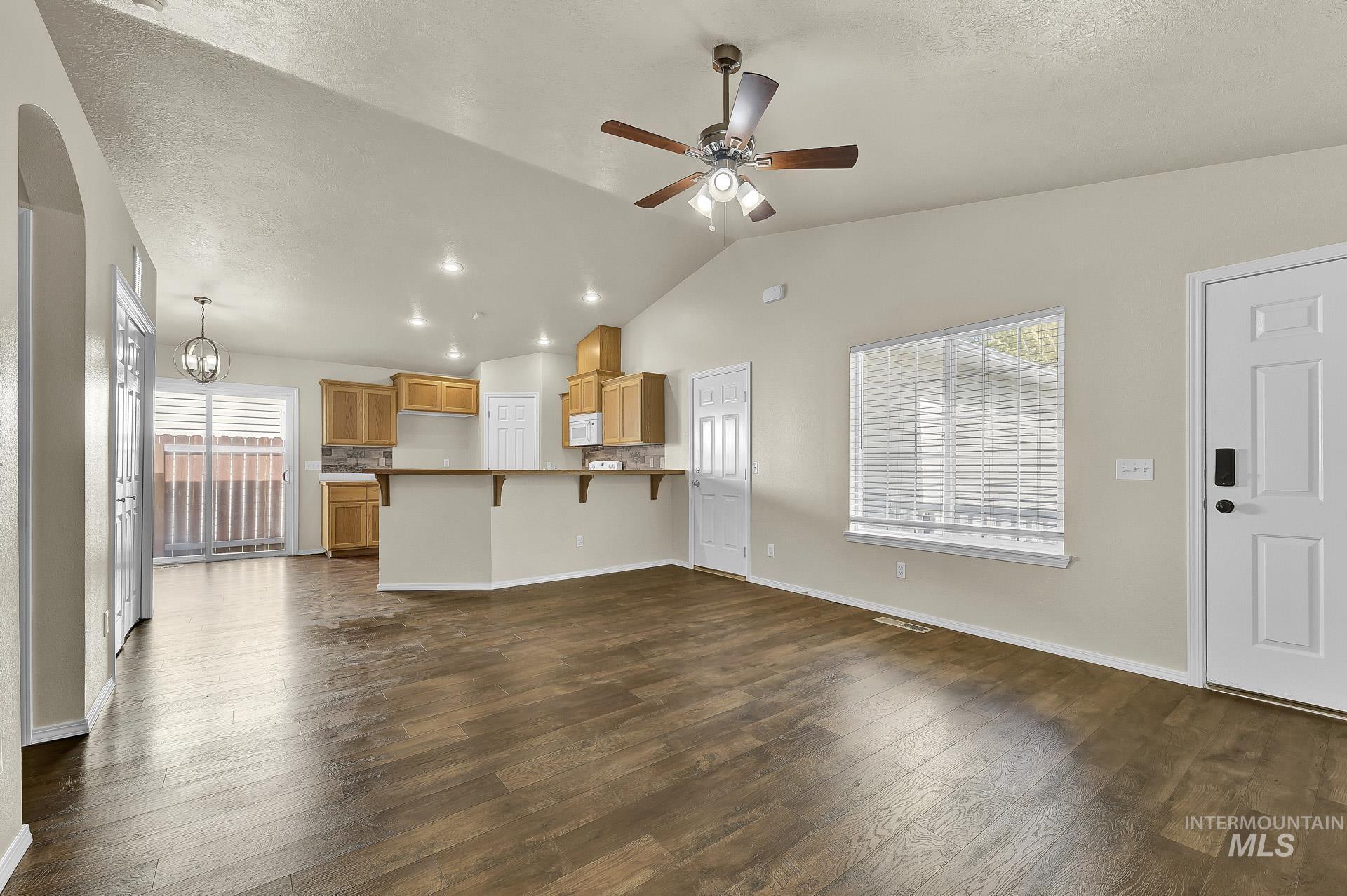 Unfurnished living room featuring healthy amount of natural light, dark wood-style flooring, lofted ceiling, ceiling fan, and a chandelier