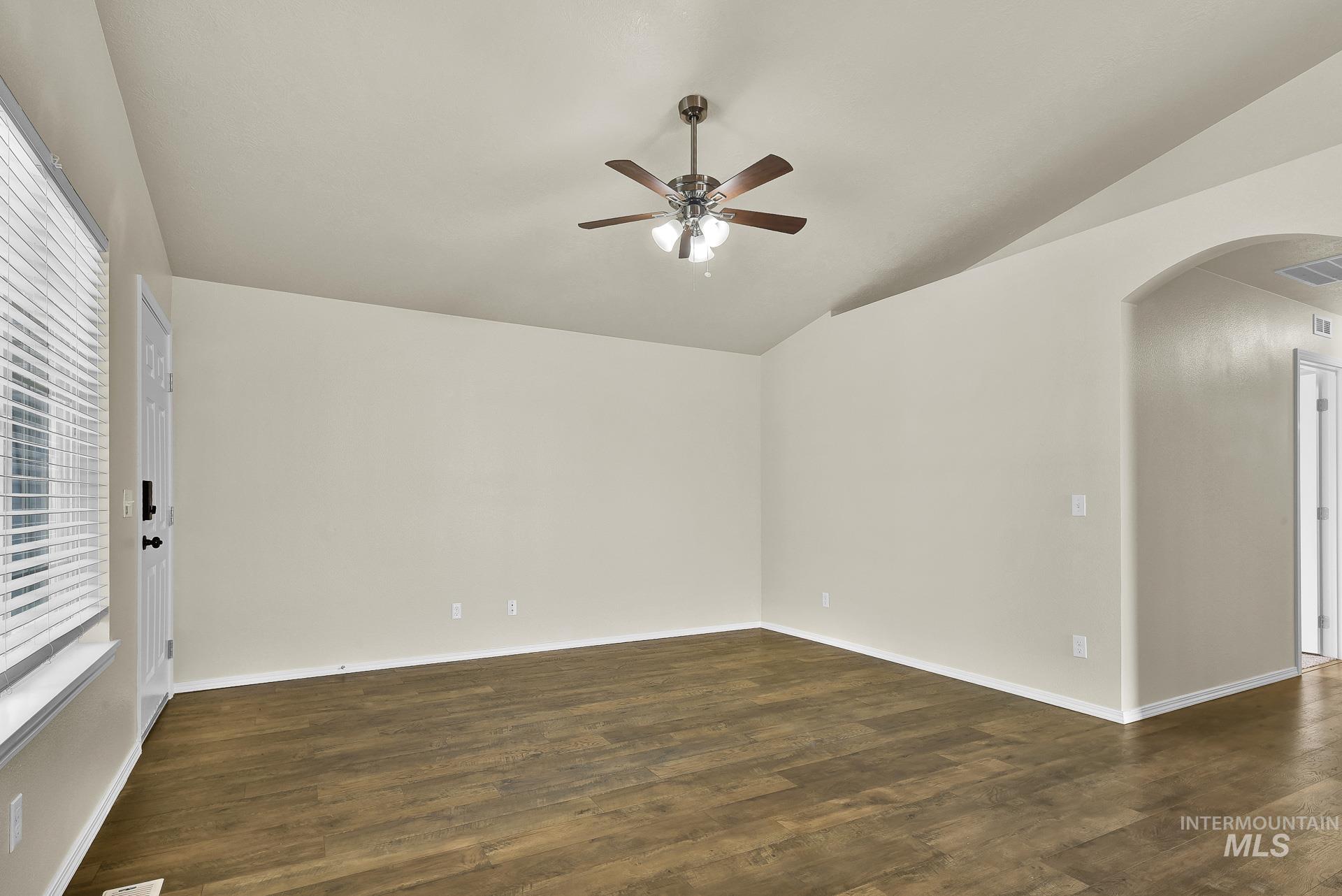 Spare room featuring arched walkways, dark wood finished floors, lofted ceiling, and a ceiling fan
