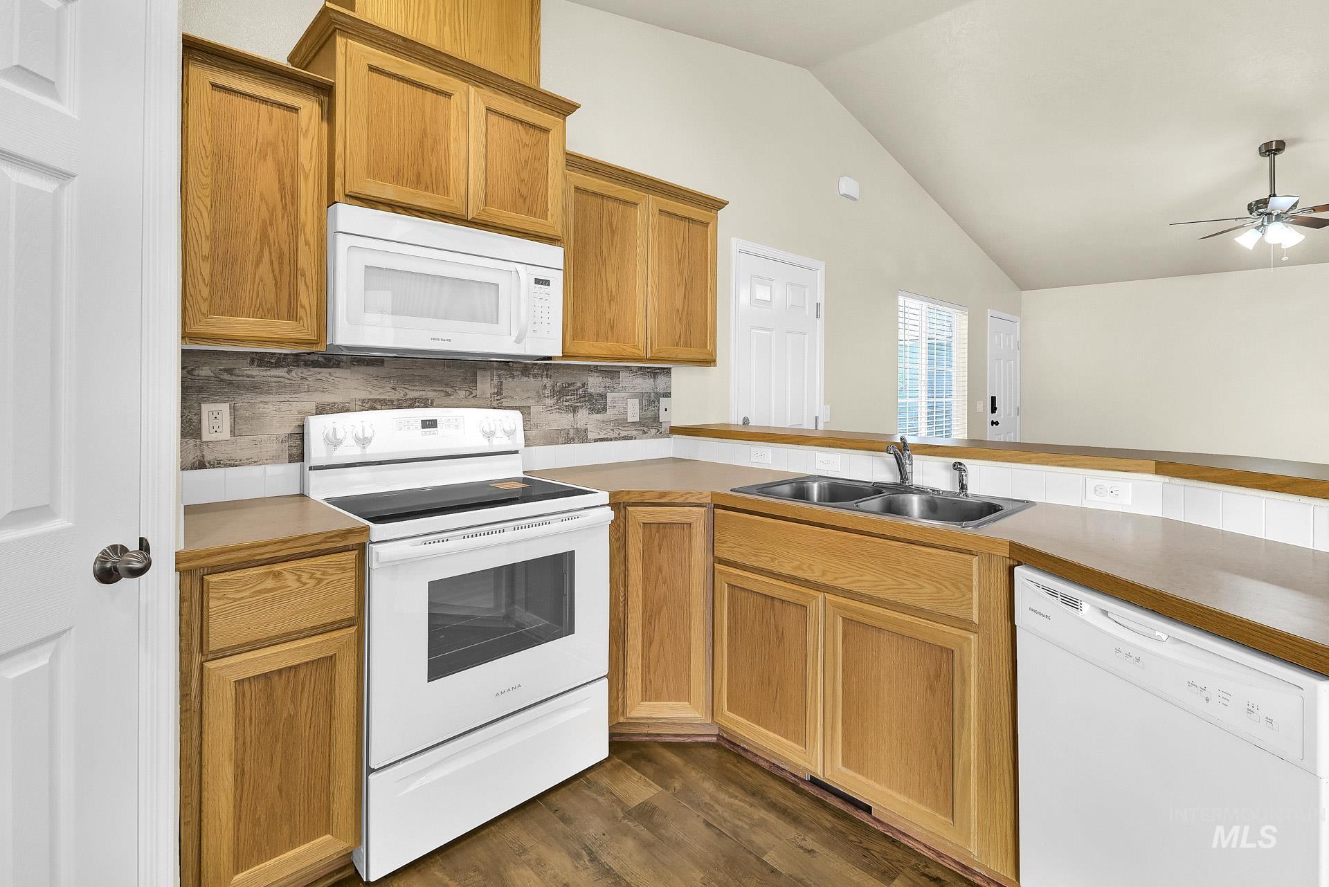 Kitchen featuring white appliances, lofted ceiling, tasteful backsplash, dark wood finished floors, and light countertops
