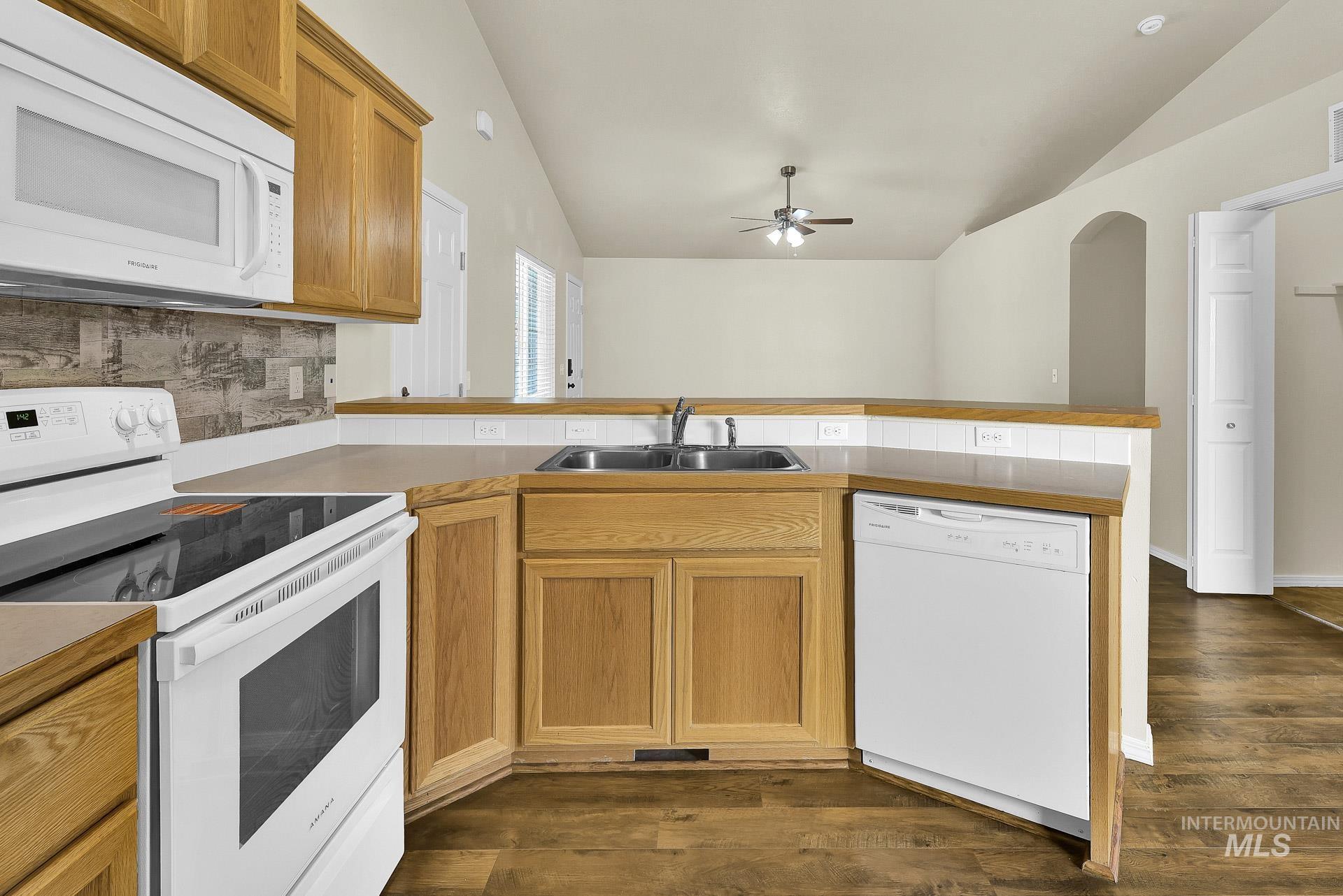 Kitchen with white appliances, vaulted ceiling, a peninsula, tasteful backsplash, and brown cabinetry
