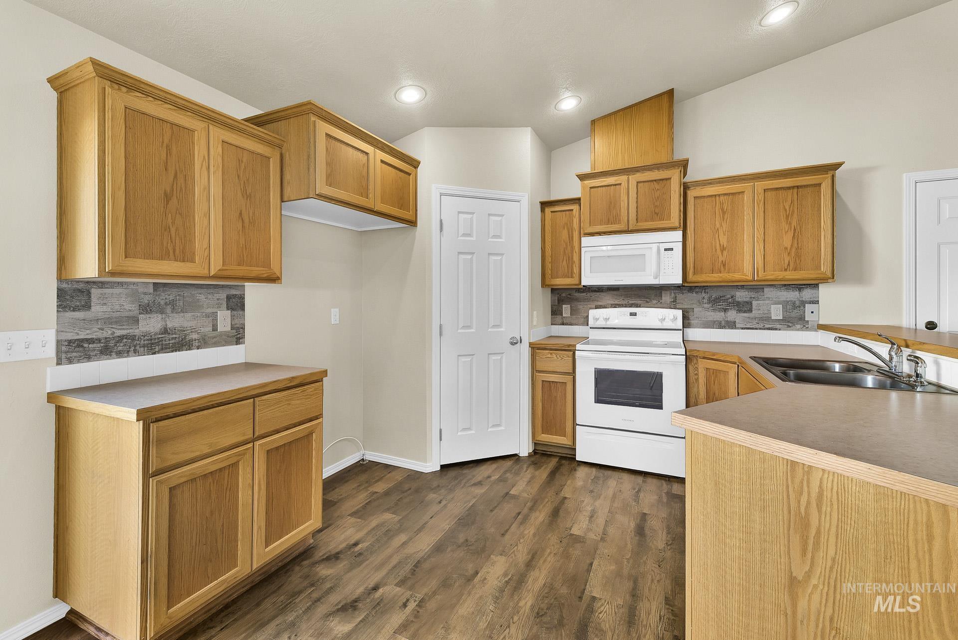 Kitchen with tasteful backsplash, white appliances, dark wood finished floors, brown cabinets, and light countertops