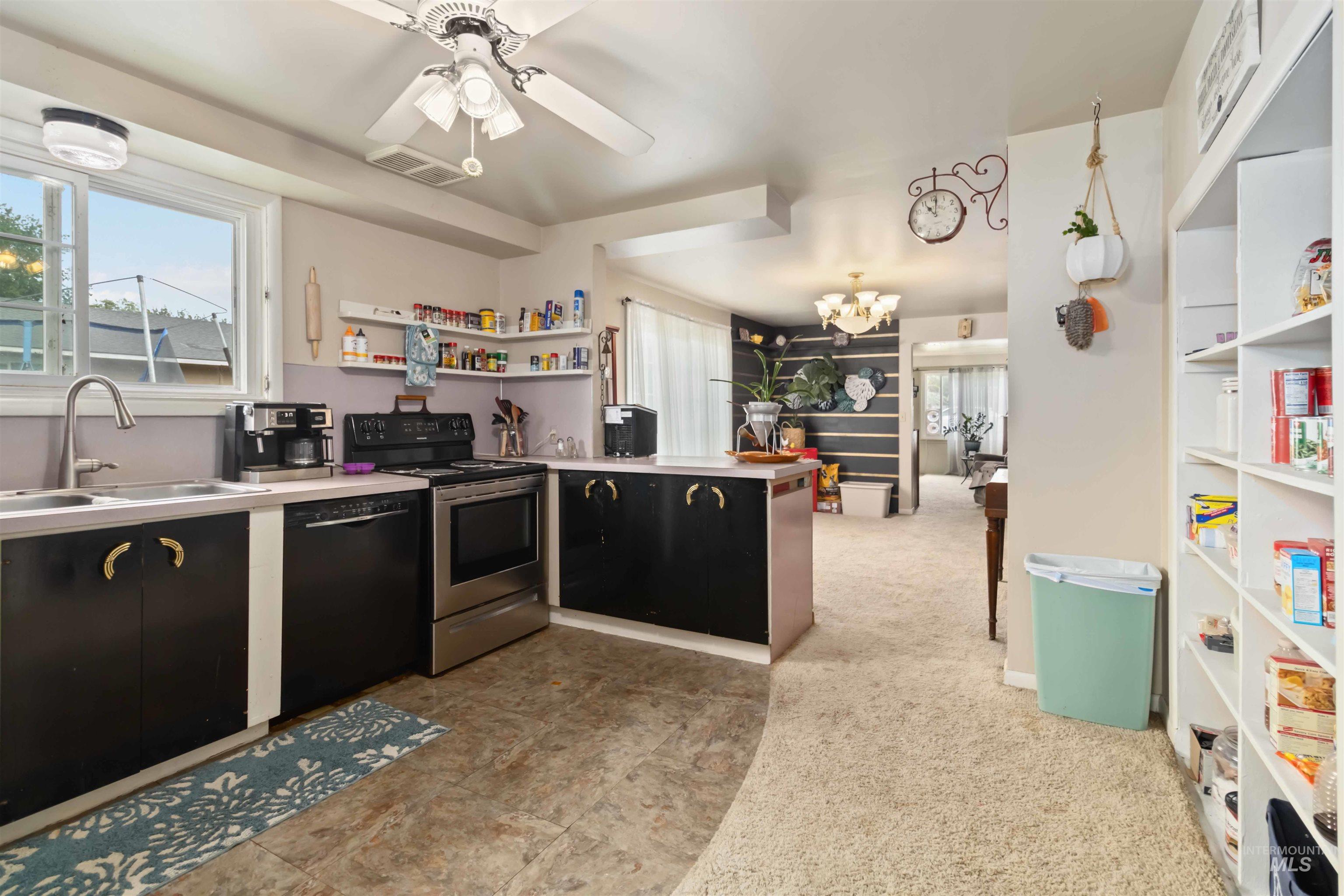 Kitchen featuring stainless steel electric stove, open shelves, light countertops, black dishwasher, and a peninsula