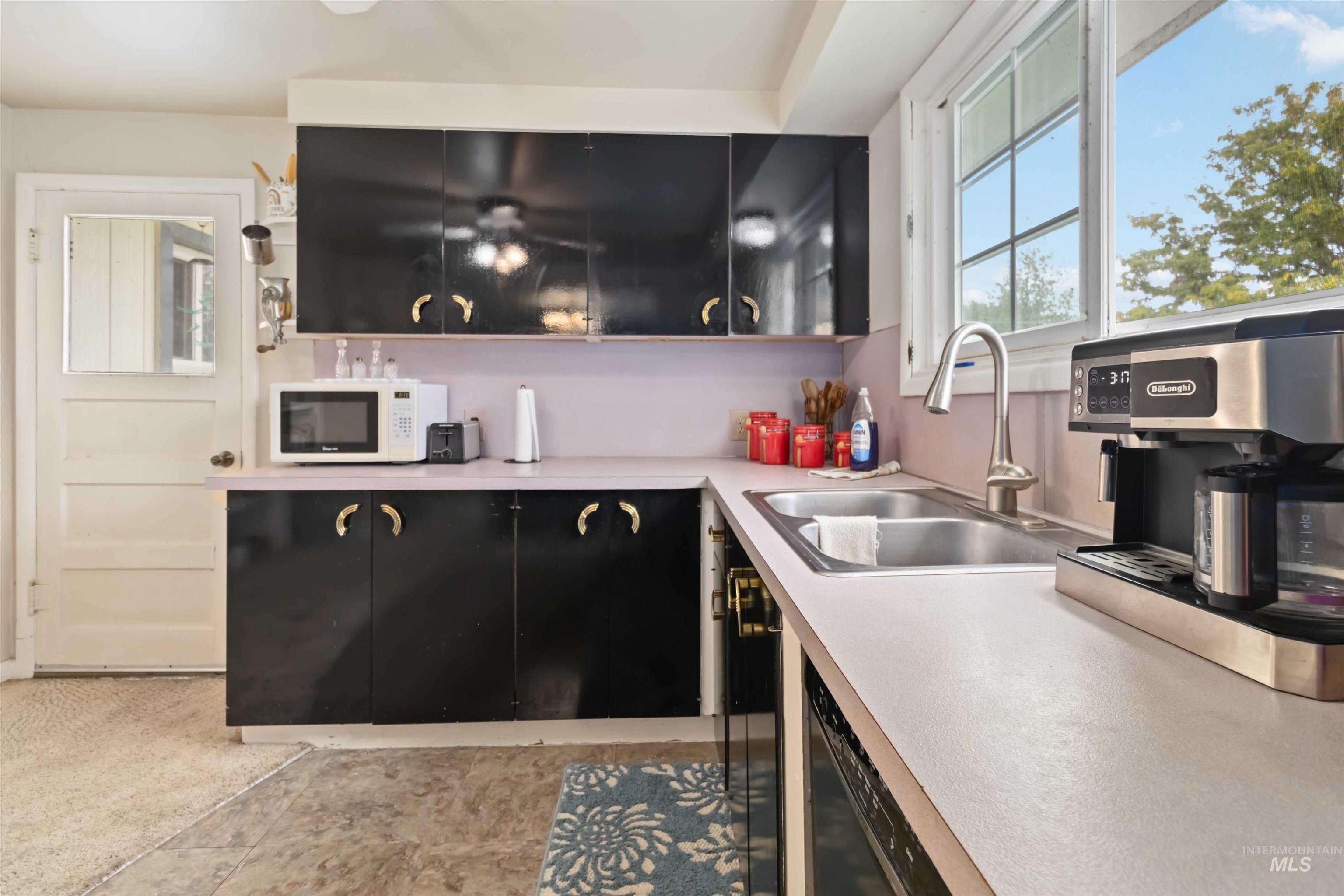 Kitchen with light countertops, white microwave, dishwasher, and dark cabinets
