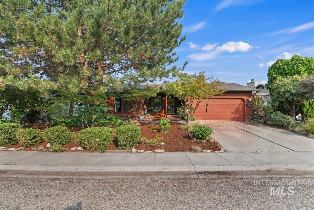 View of property hidden behind natural elements with driveway, an attached garage, and a porch