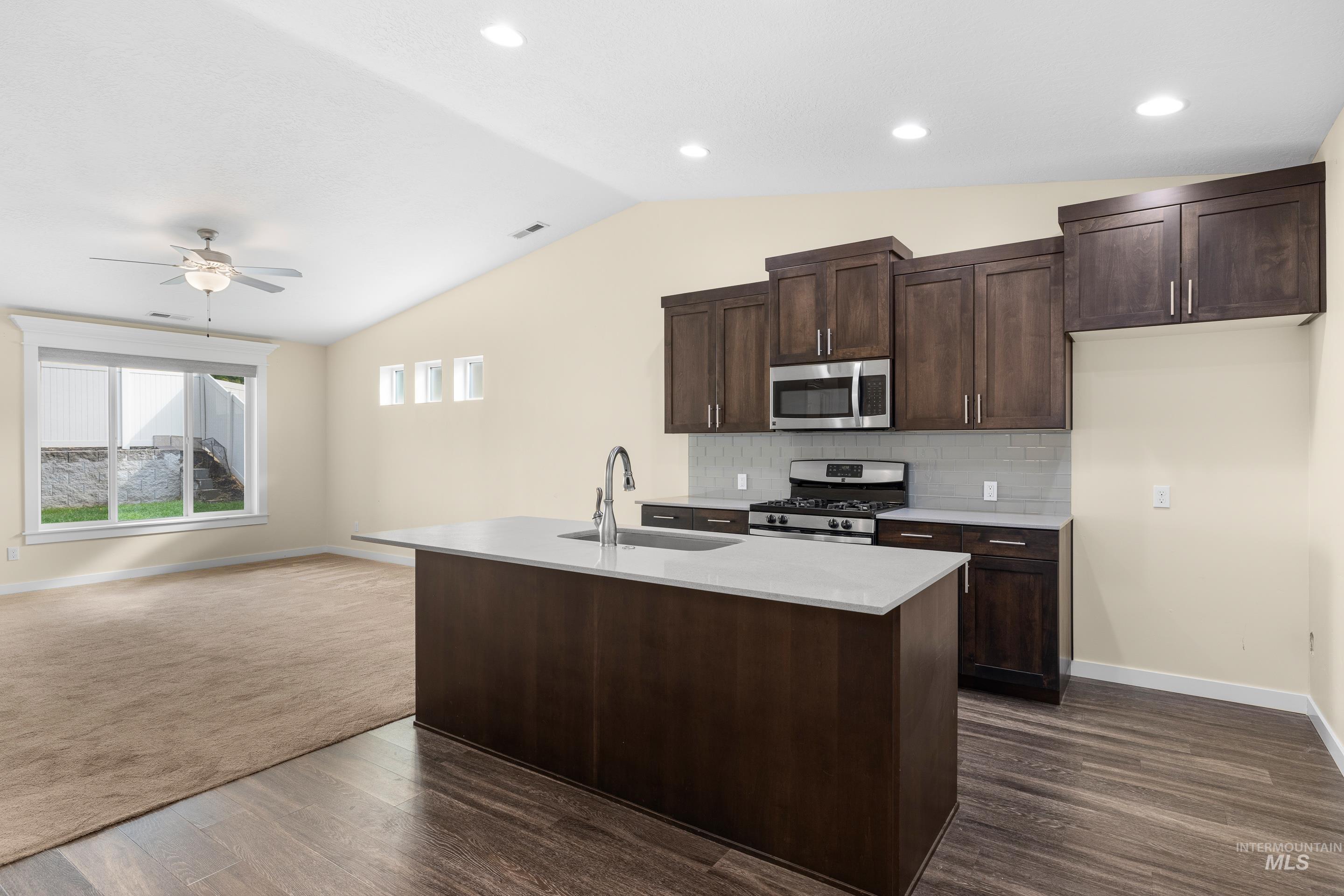 Kitchen featuring open floor plan, dark brown cabinetry, appliances with stainless steel finishes, lofted ceiling, and decorative backsplash