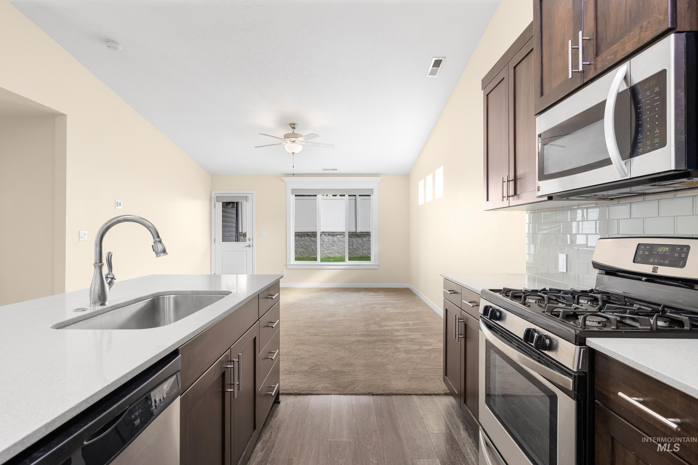 Kitchen with appliances with stainless steel finishes, dark brown cabinets, dark wood finished floors, light stone counters, and tasteful backsplash