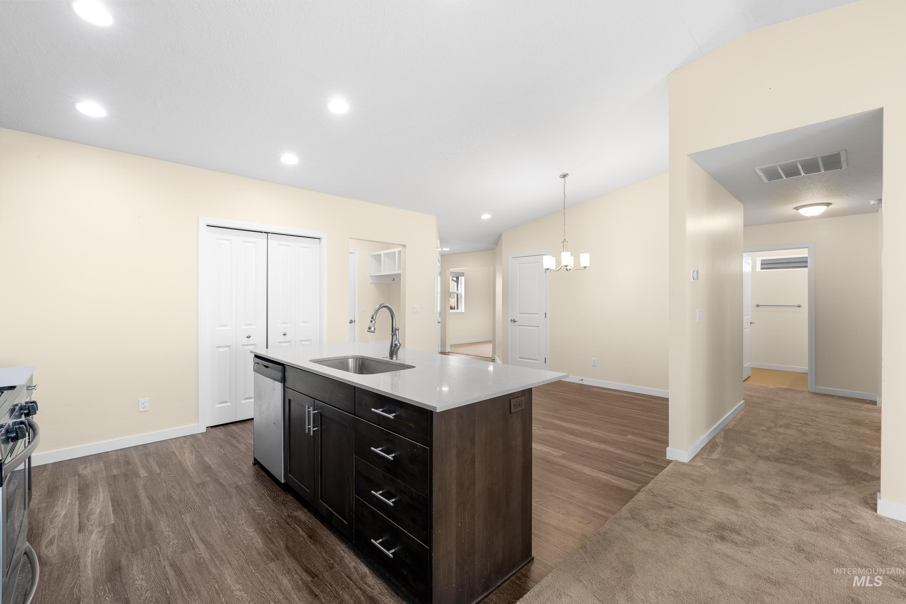 Kitchen featuring dark brown cabinetry, recessed lighting, pendant lighting, a center island with sink, and dark wood-style floors
