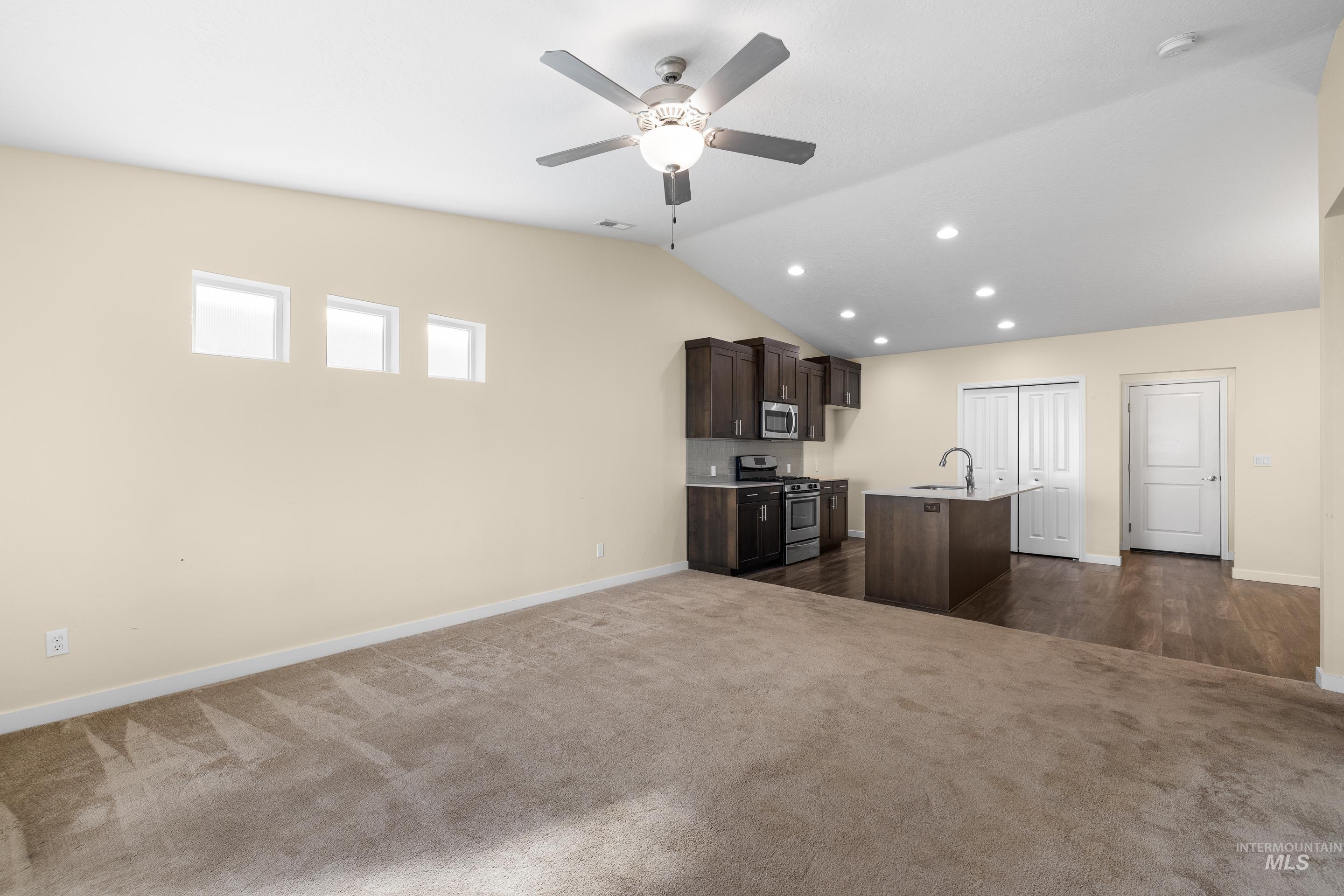 Kitchen with dark brown cabinetry, dark carpet, a center island with sink, open floor plan, and lofted ceiling