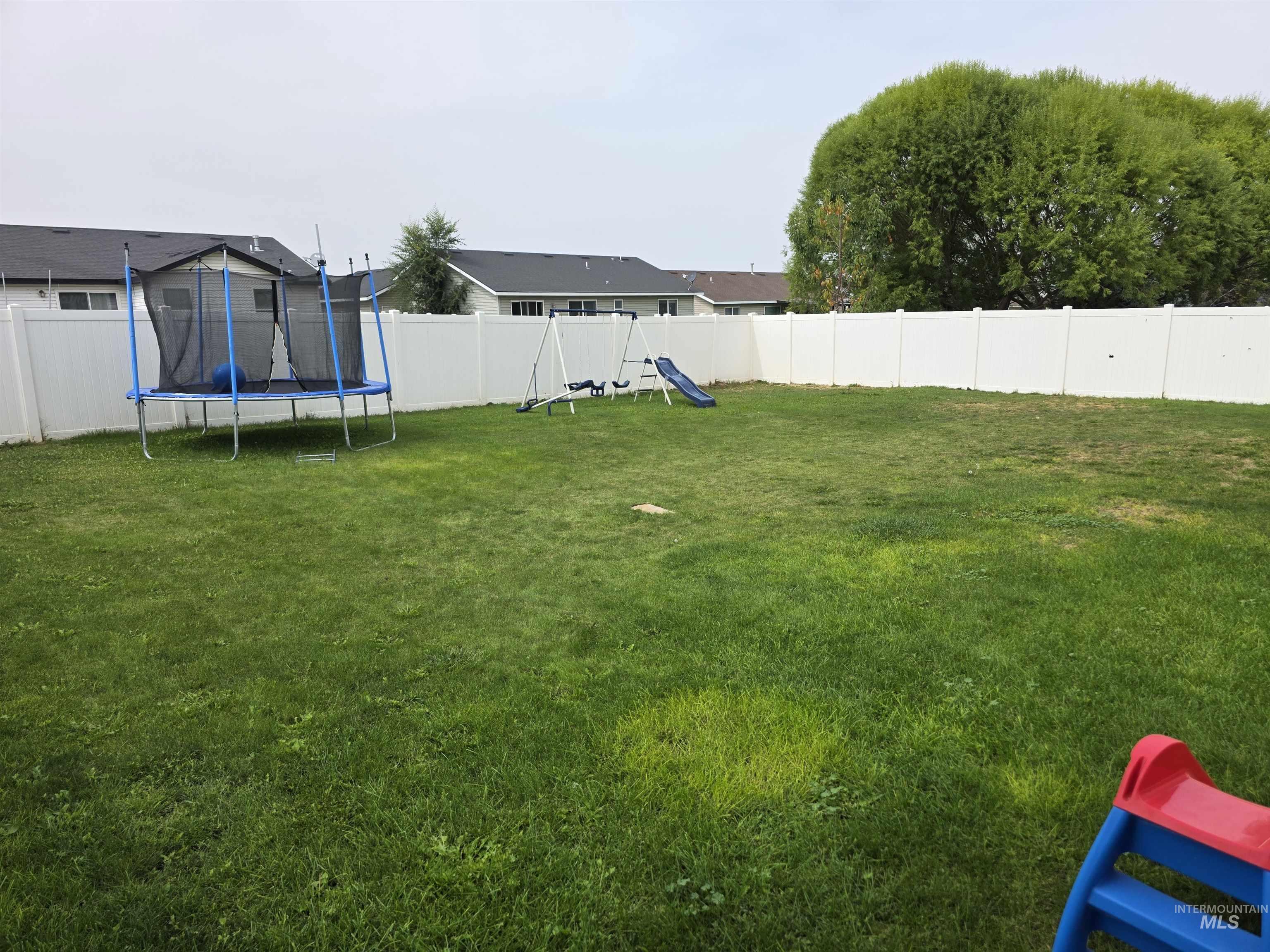 Fenced backyard featuring a playground and a trampoline