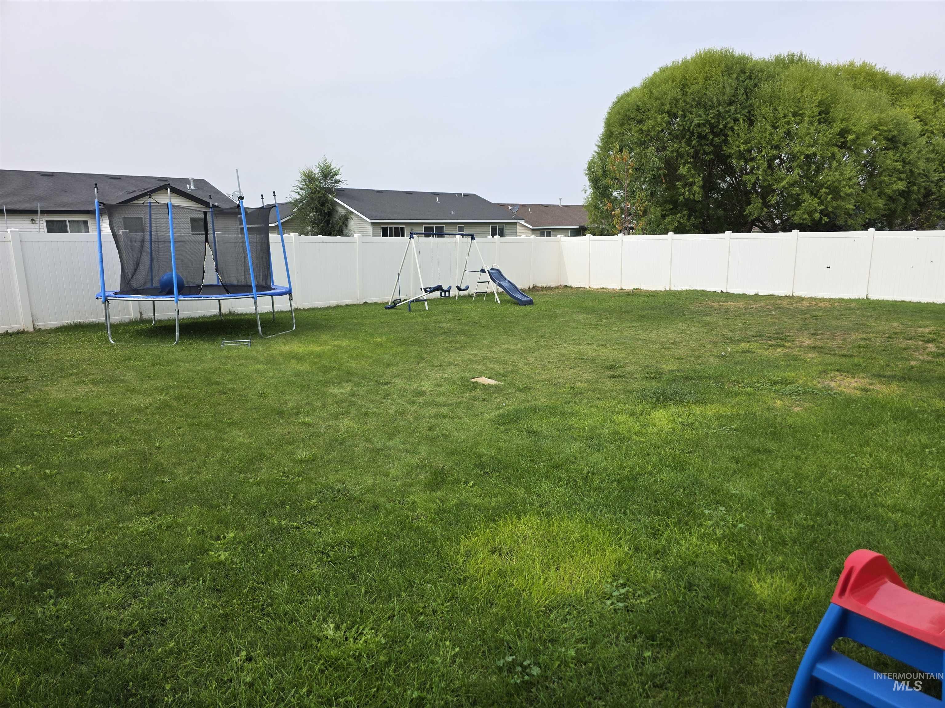Fenced backyard featuring a playground and a trampoline