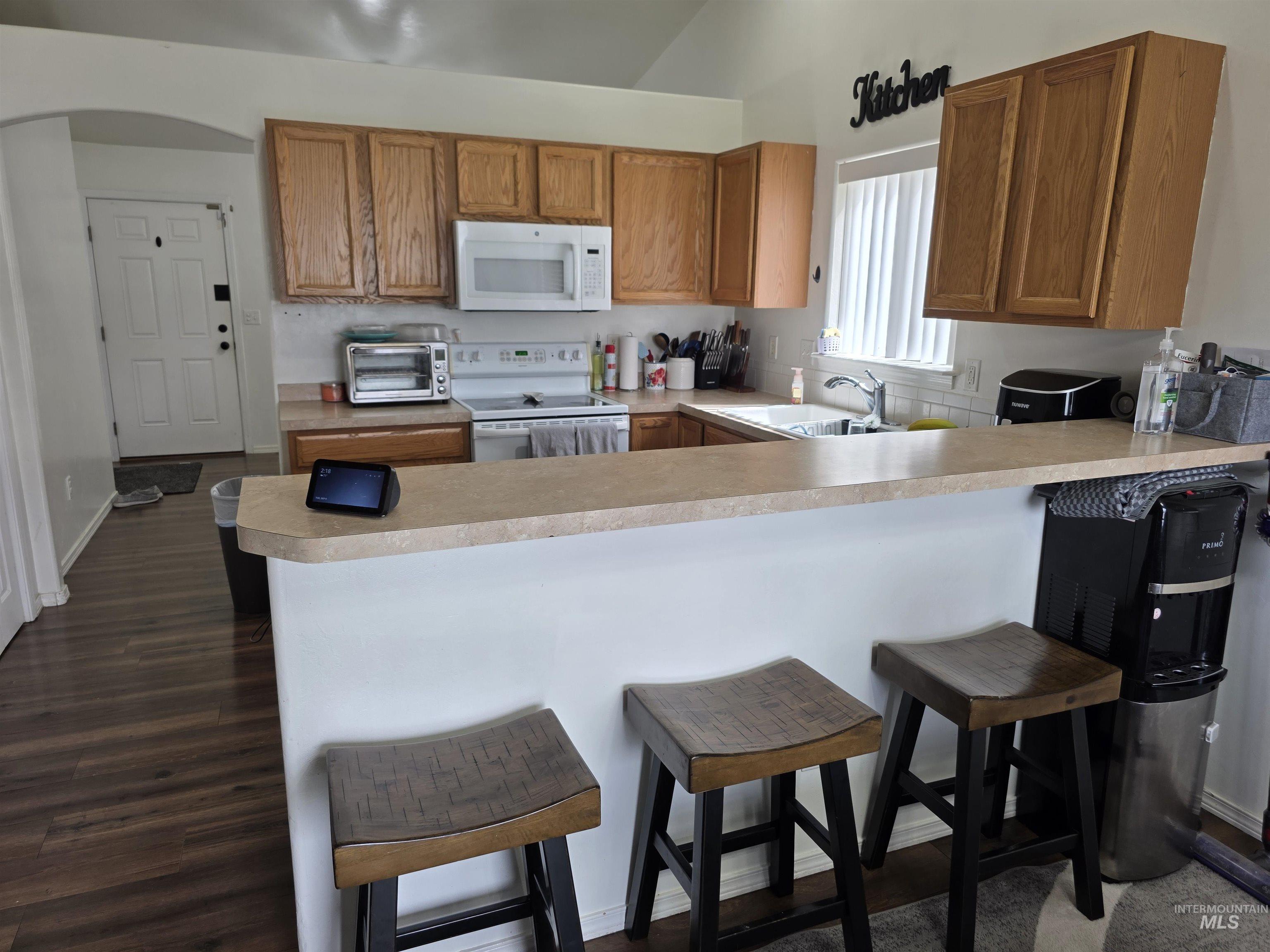 Kitchen featuring light countertops, a breakfast bar area, white appliances, a peninsula, and brown cabinetry