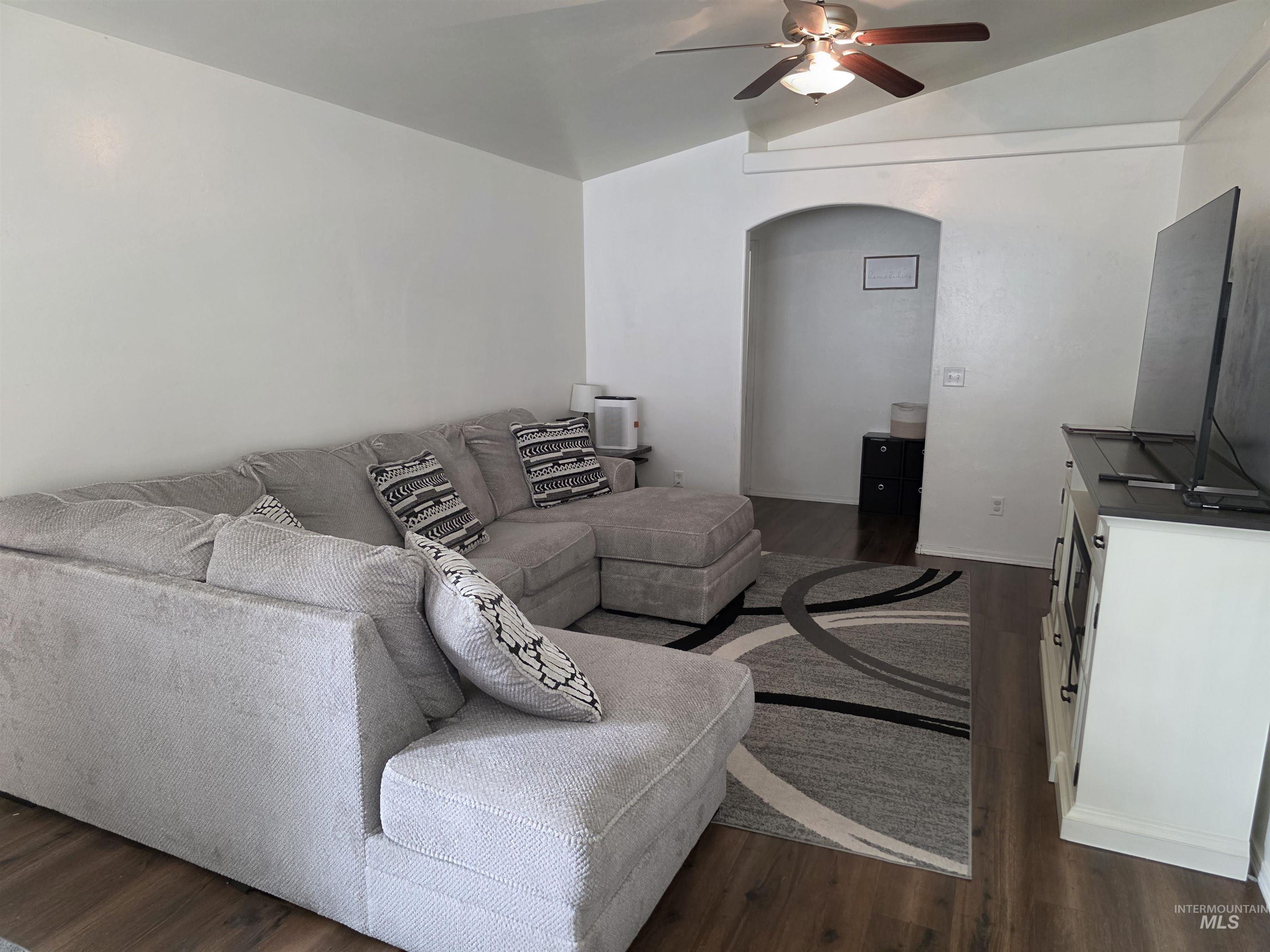 Living room featuring arched walkways, dark wood-style floors, lofted ceiling, and ceiling fan
