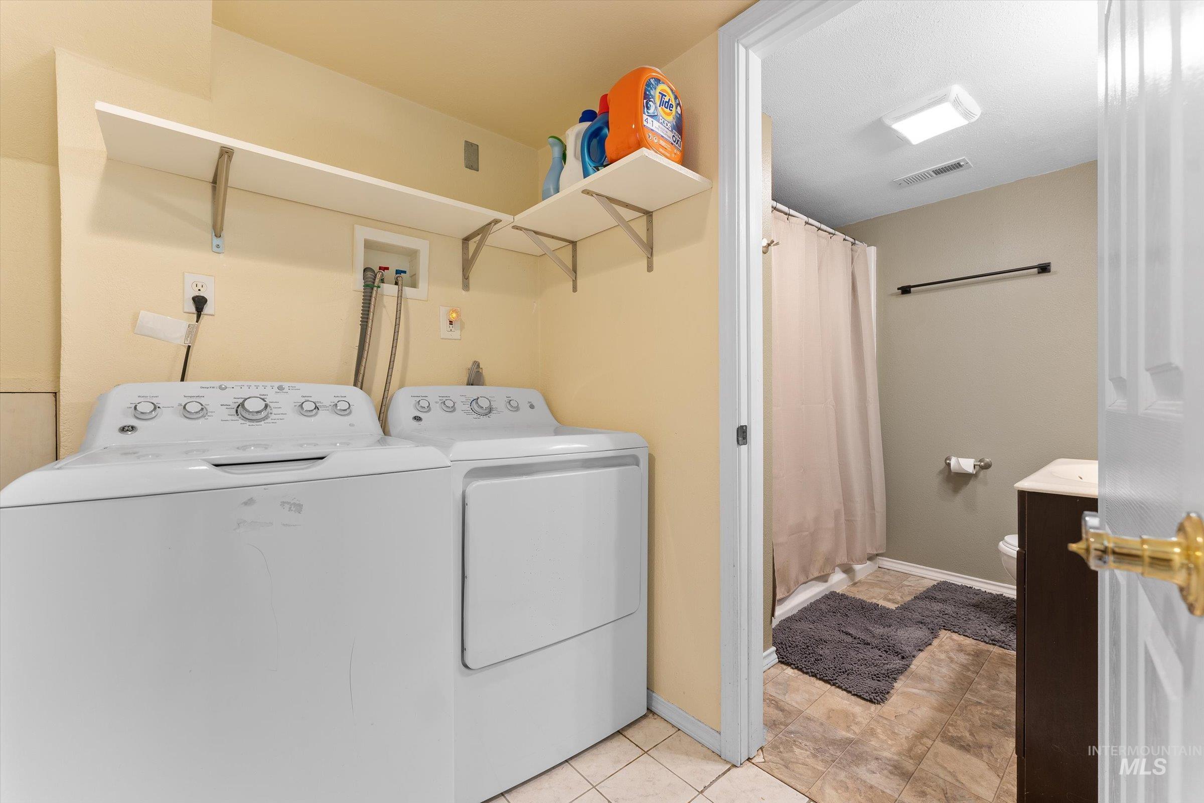 Laundry room with washer and clothes dryer and light tile patterned flooring