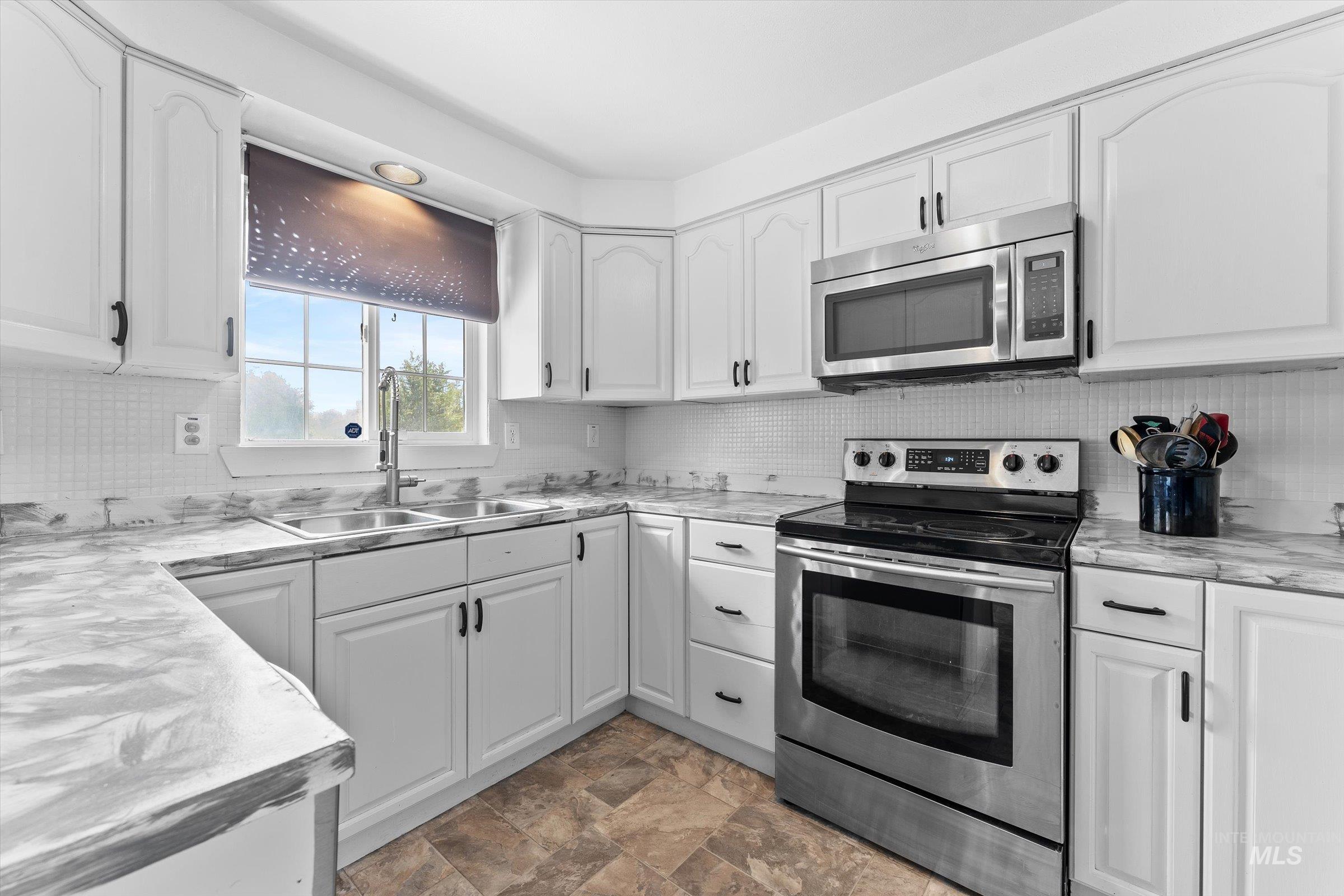 Kitchen featuring appliances with stainless steel finishes, white cabinets, stone finish floors, and backsplash