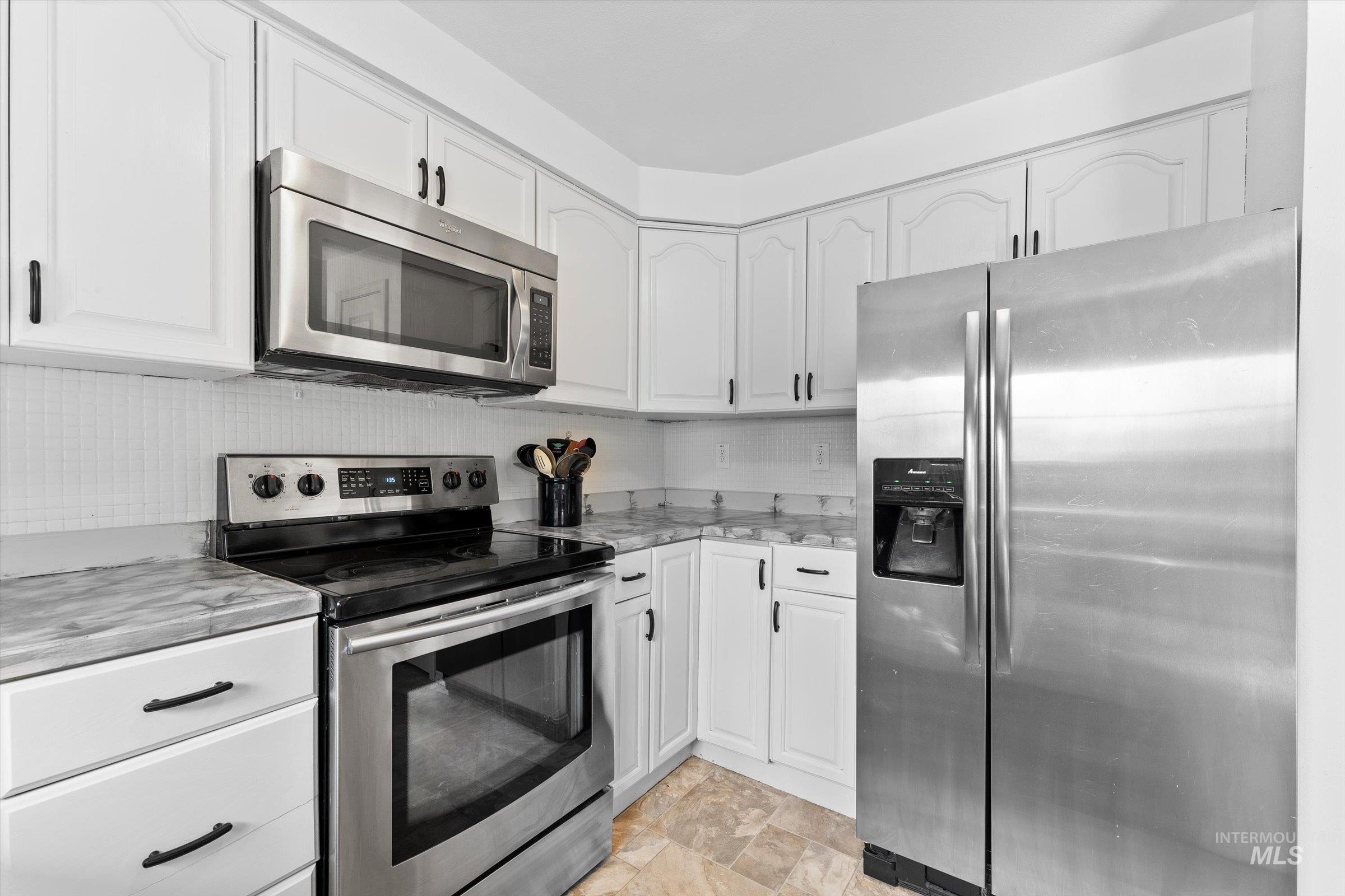 Kitchen featuring appliances with stainless steel finishes, backsplash, white cabinets, and stone finish flooring