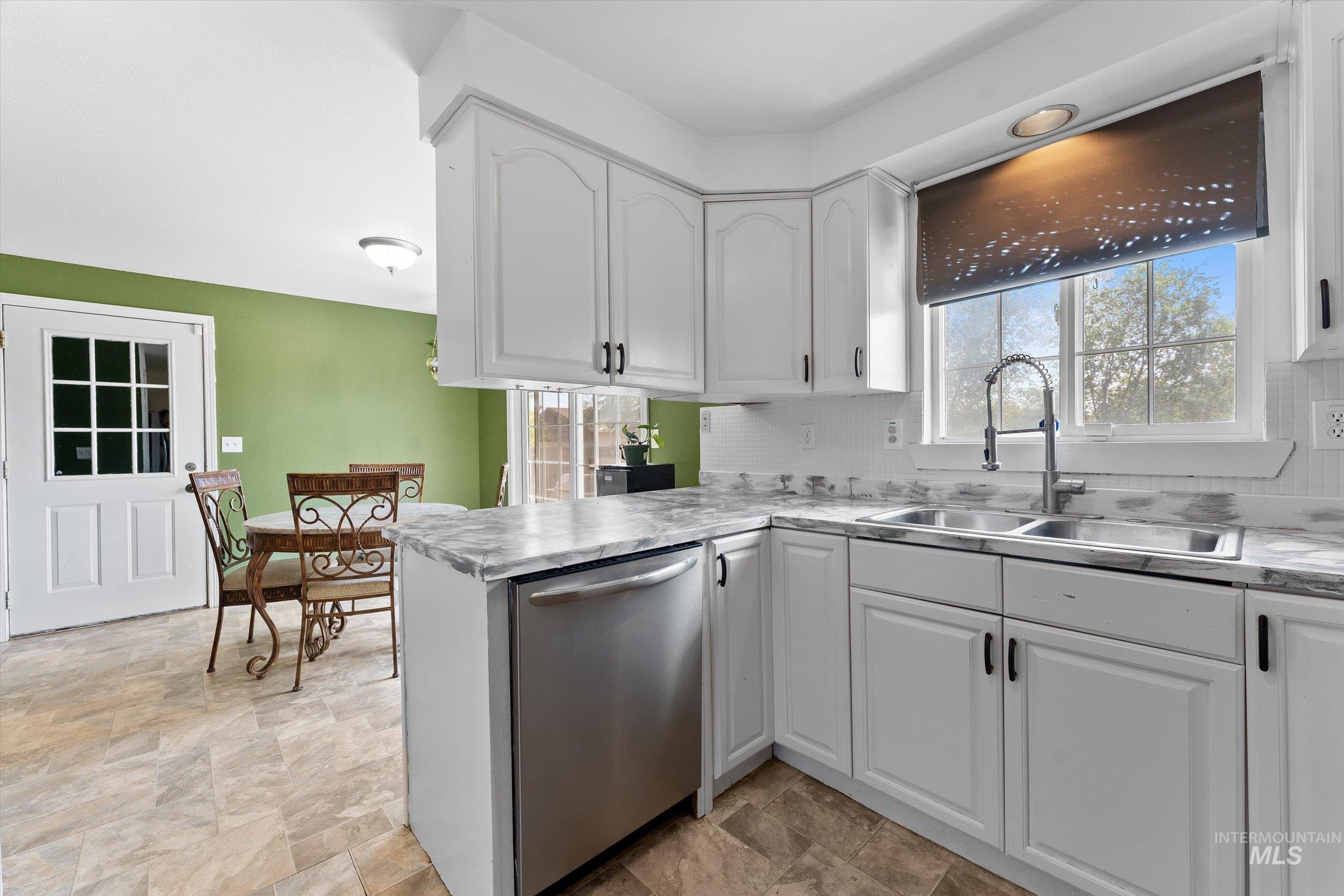 Kitchen with white cabinetry, dishwasher, stone finish floors, tasteful backsplash, and light countertops
