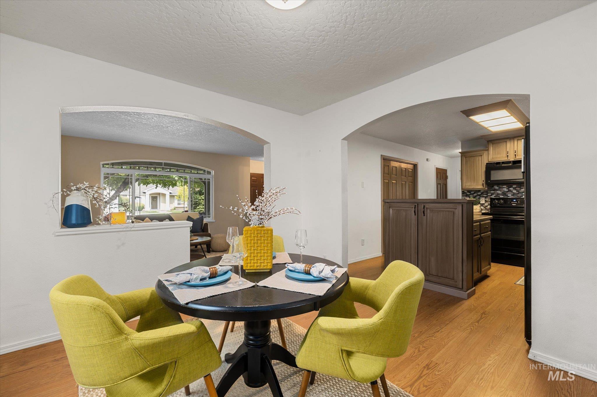 Dining space featuring a textured ceiling, arched walkways, and light wood-style flooring