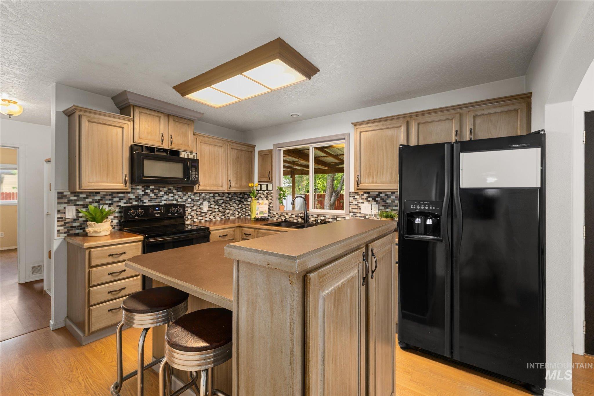 Kitchen with black appliances, light wood finished floors, a textured ceiling, a kitchen bar, and light countertops