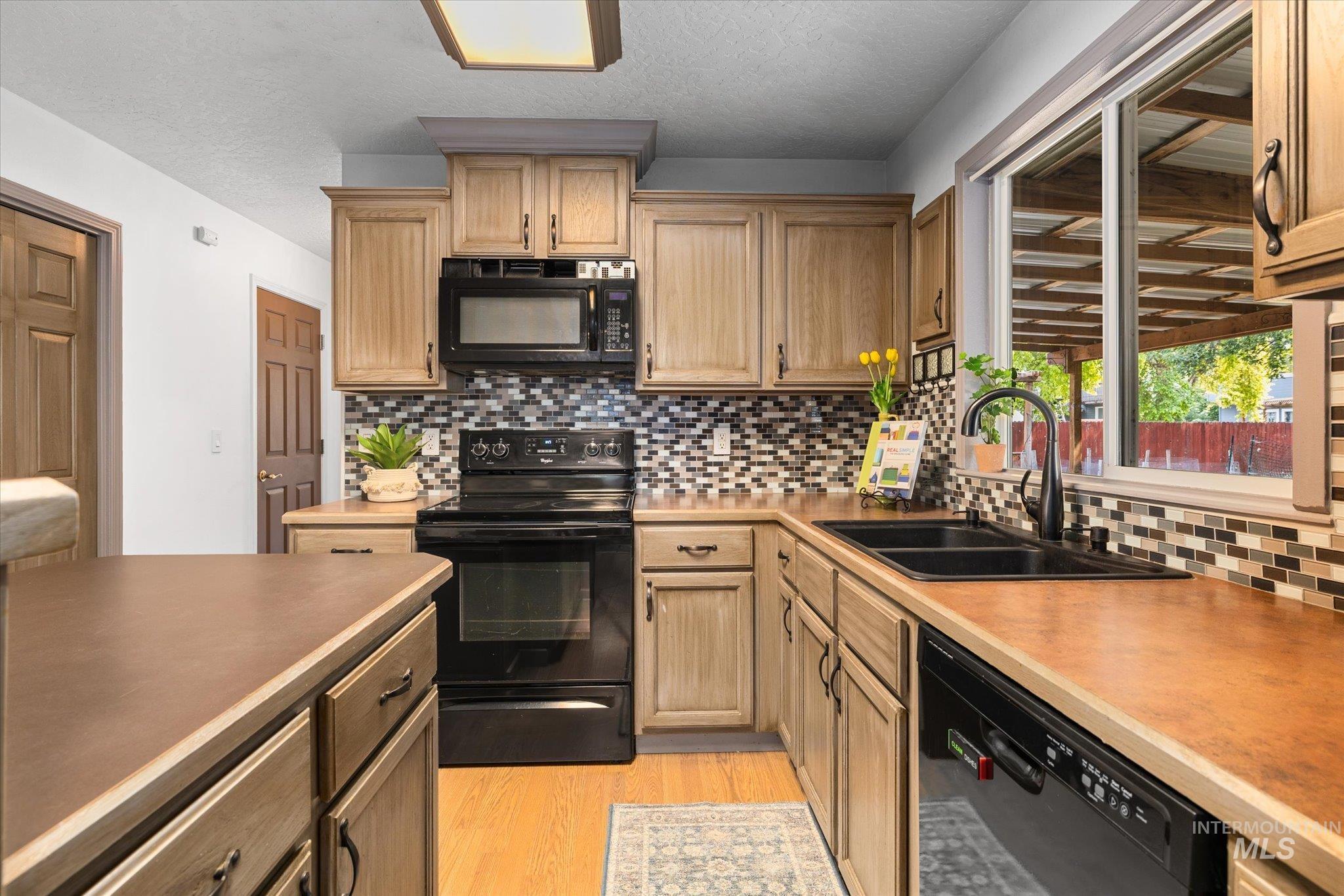 Kitchen featuring black appliances, decorative backsplash, light wood-style floors, light countertops, and a textured ceiling