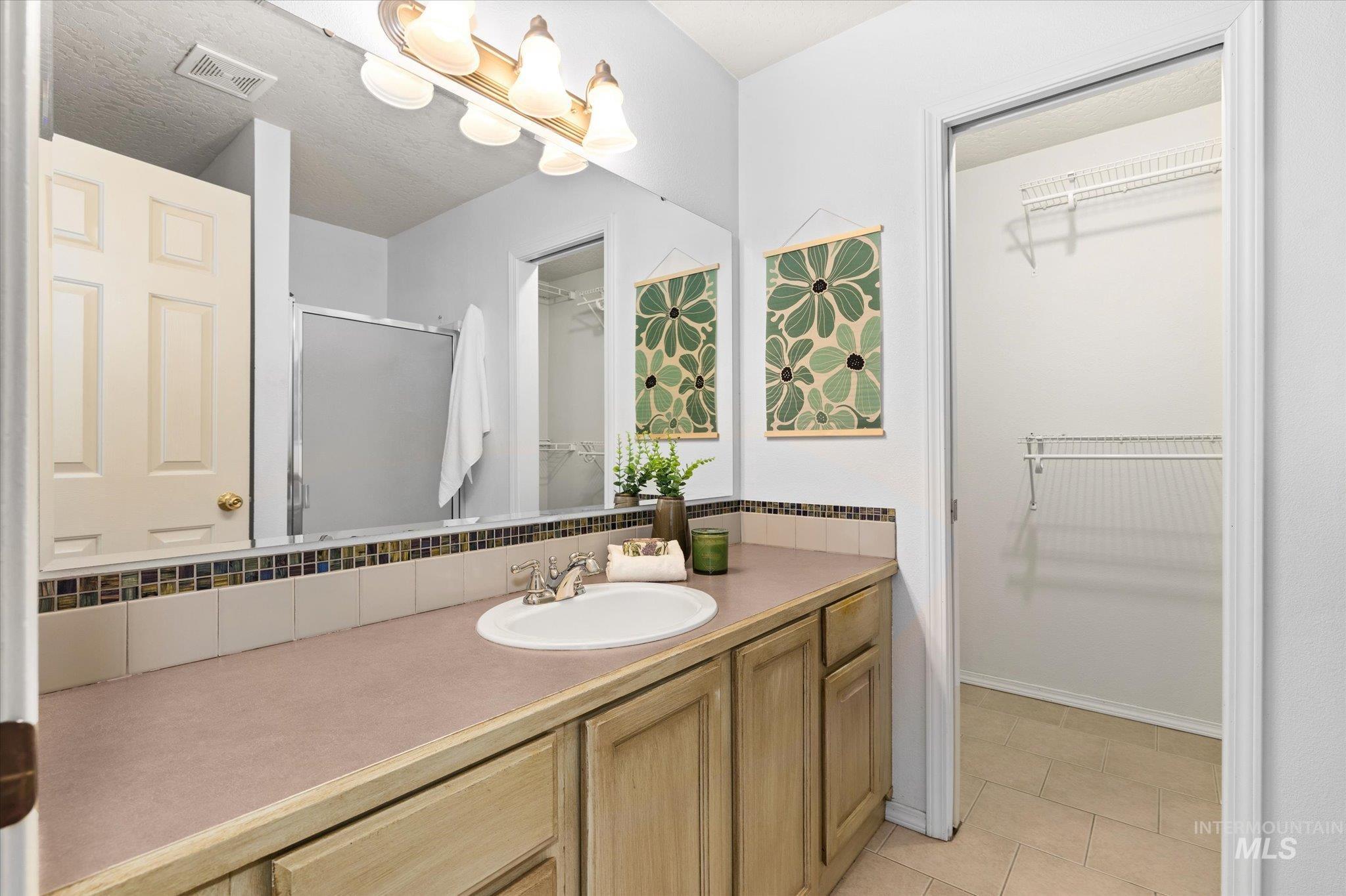 Full bath with a walk in closet, vanity, a shower stall, and light tile patterned flooring