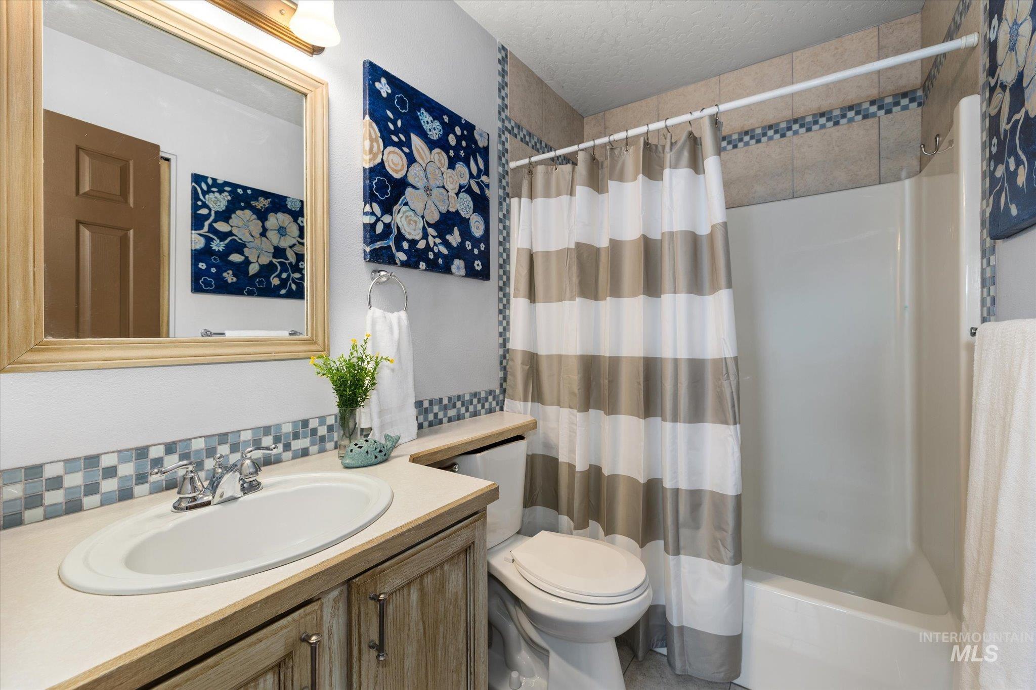 Full bathroom featuring vanity, shower / tub combo, backsplash, and a textured ceiling
