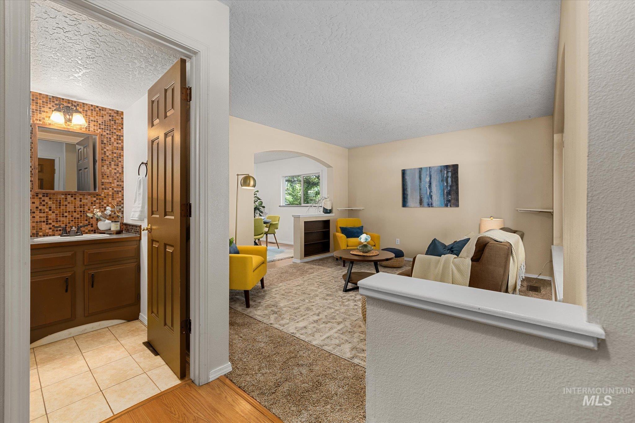 Living area with light wood-style floors, arched walkways, a textured ceiling, and light colored carpet