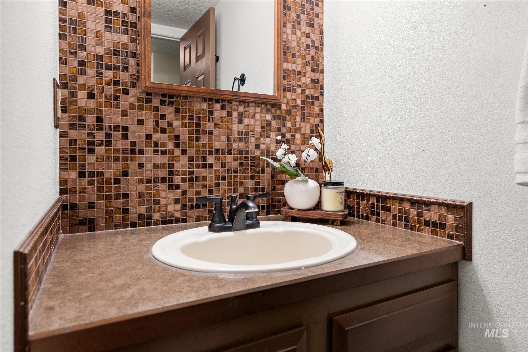 Bathroom featuring a textured wall, decorative backsplash, and vanity