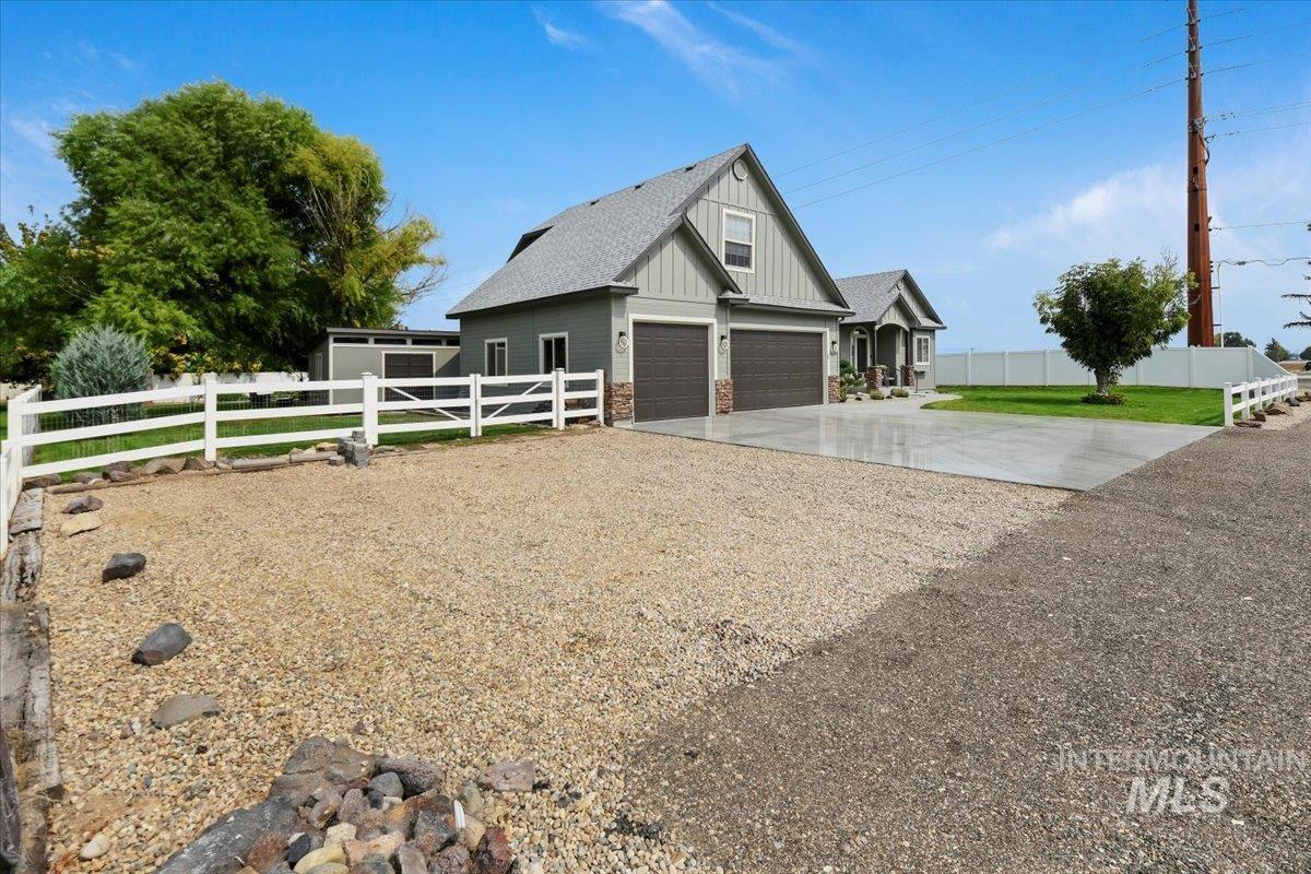 View of side of property featuring driveway, board and batten siding, a garage, roof with shingles, and stone siding