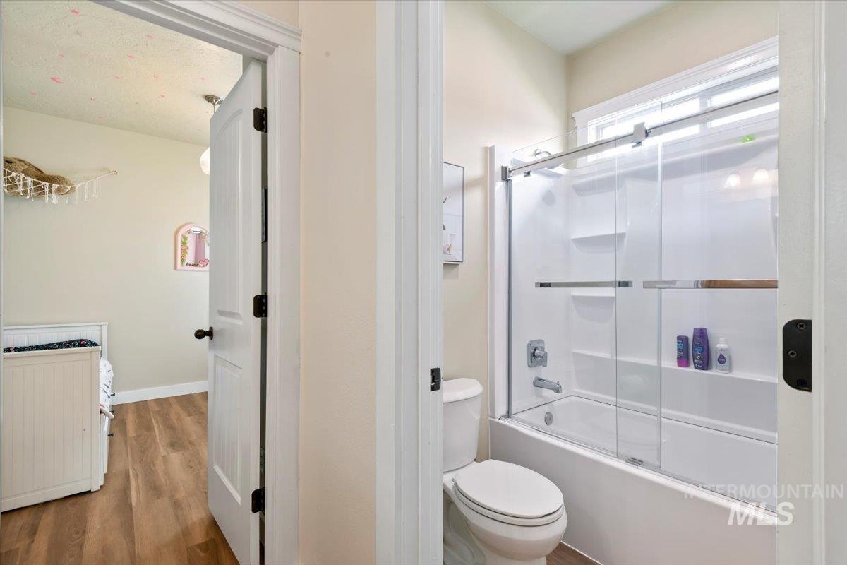 Full bath with combined bath / shower with glass door and wood finished floors