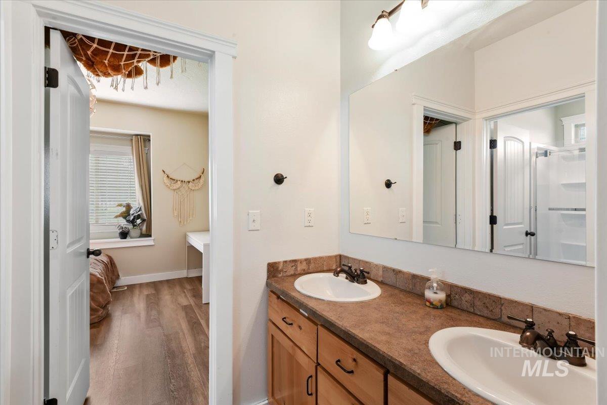 Full bath featuring double vanity, dark wood finished floors, and a shower with door