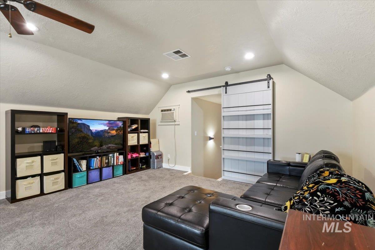 Carpeted living area featuring a barn door, a textured ceiling, lofted ceiling, recessed lighting, and a wall mounted AC