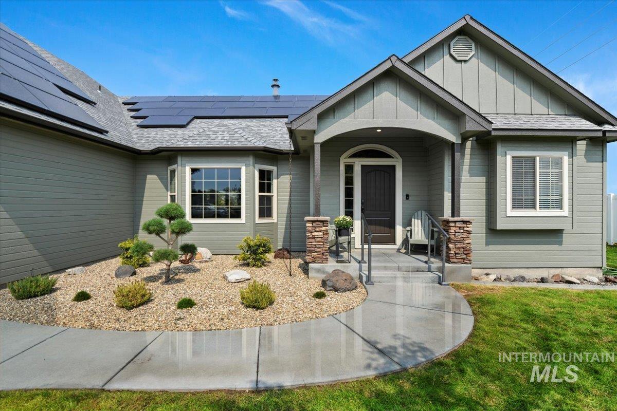 View of front of house with roof mounted solar panels, board and batten siding, a shingled roof, and a front yard