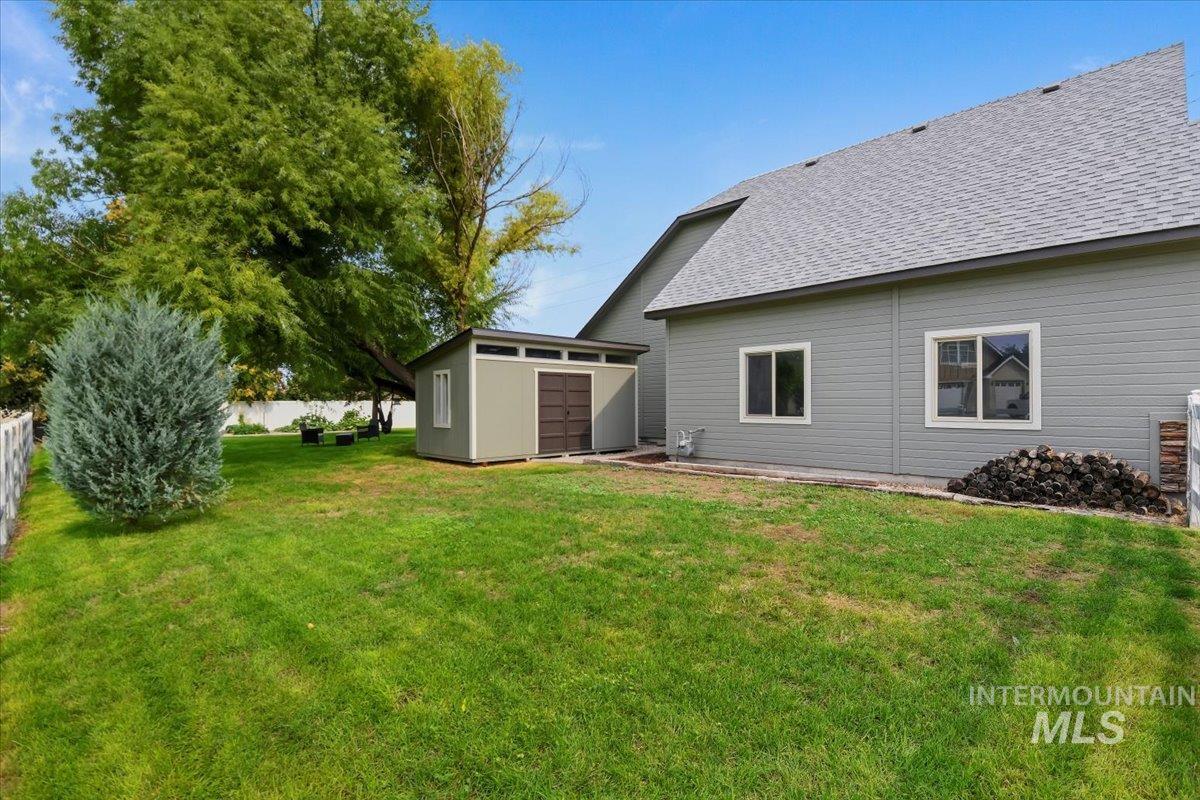 Back of property with a shingled roof, a shed, and a lawn