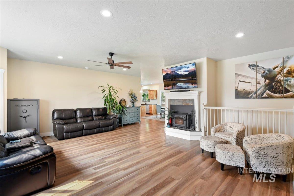 Living area with light wood-style floors, a wood stove, a textured ceiling, recessed lighting, and ceiling fan