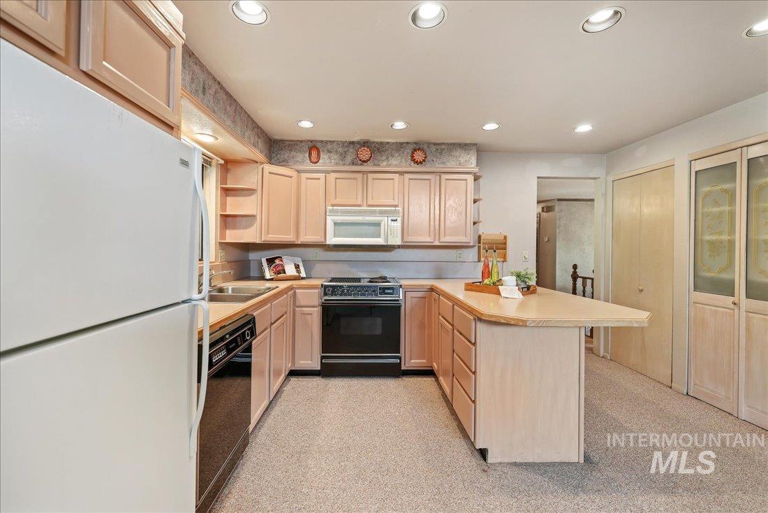 Kitchen with open shelves, white appliances, a peninsula, light countertops, and light brown cabinets