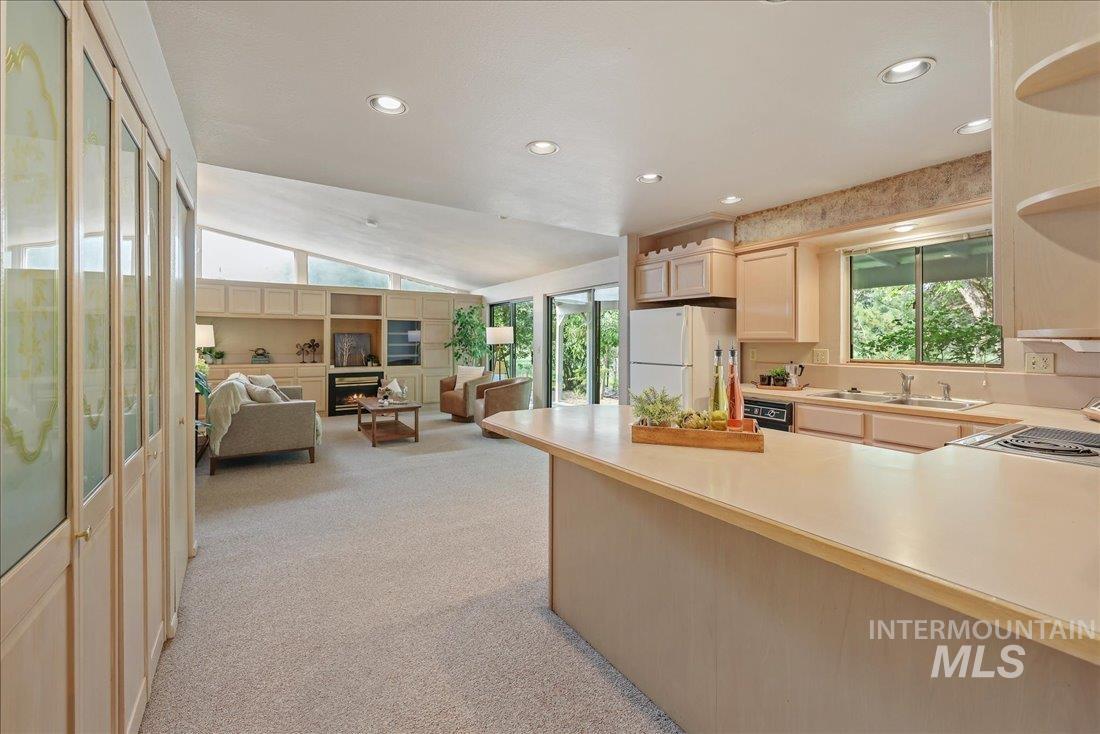 Kitchen featuring light countertops, light colored carpet, light brown cabinets, freestanding refrigerator, and vaulted ceiling