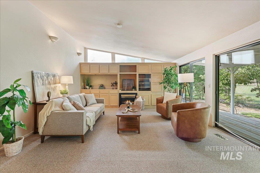 Living area with light carpet, a lit fireplace, and vaulted ceiling