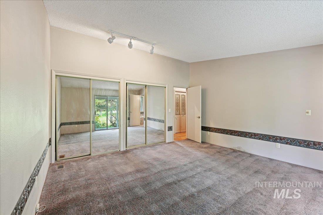 Unfurnished bedroom with multiple closets, carpet floors, rail lighting, and a textured ceiling