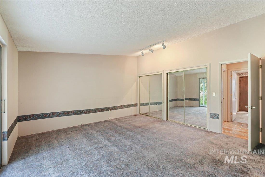 Unfurnished bedroom featuring two closets, carpet, rail lighting, and a textured ceiling