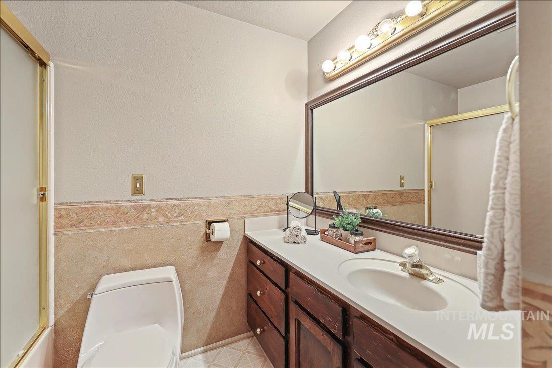 Full bathroom featuring vanity, a shower with shower door, wainscoting, and tile walls
