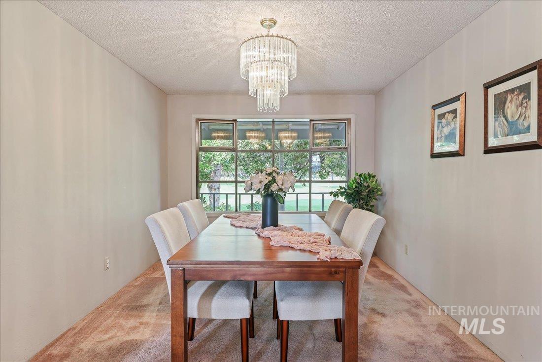 Carpeted dining space featuring a textured ceiling and a chandelier