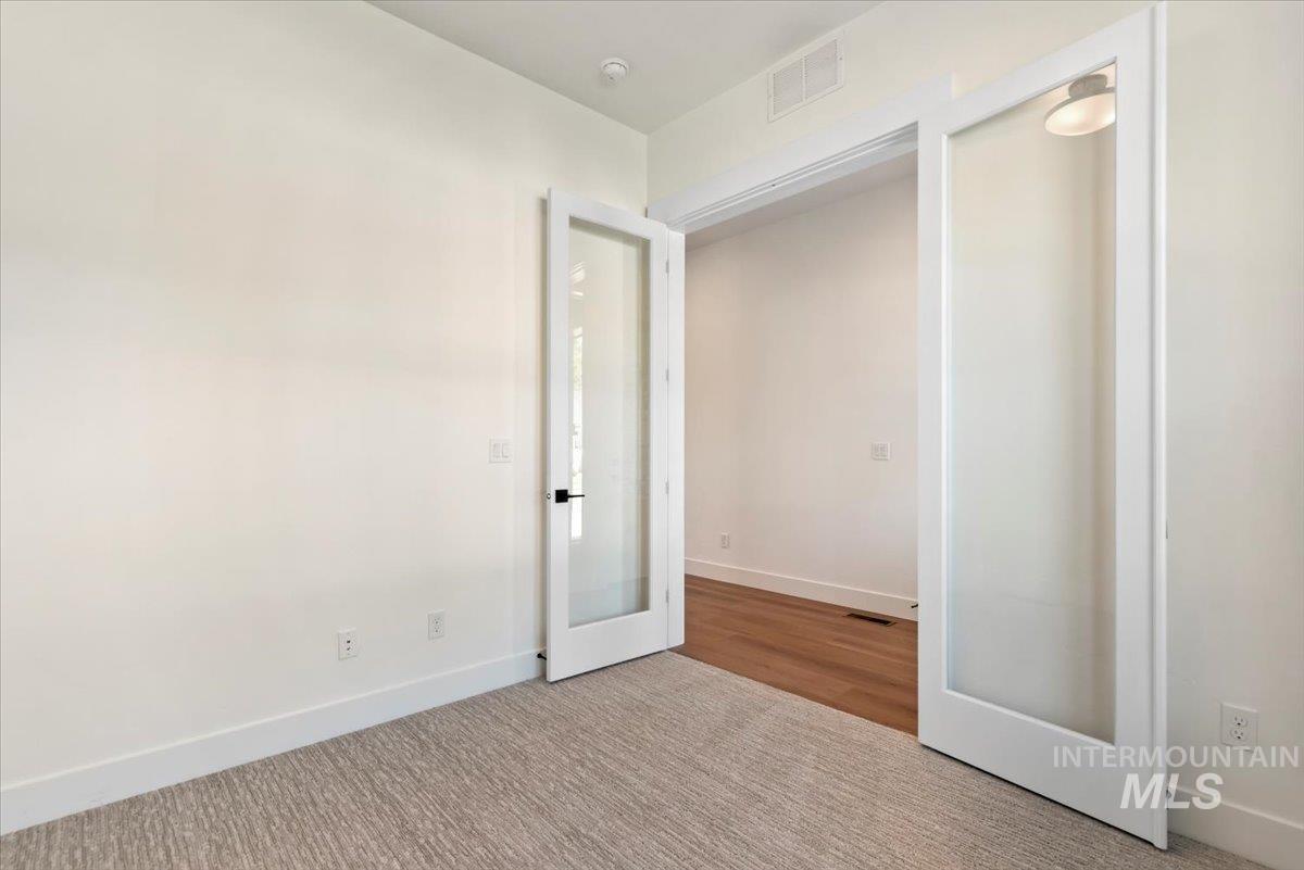 Carpeted spare room featuring baseboards and french doors
