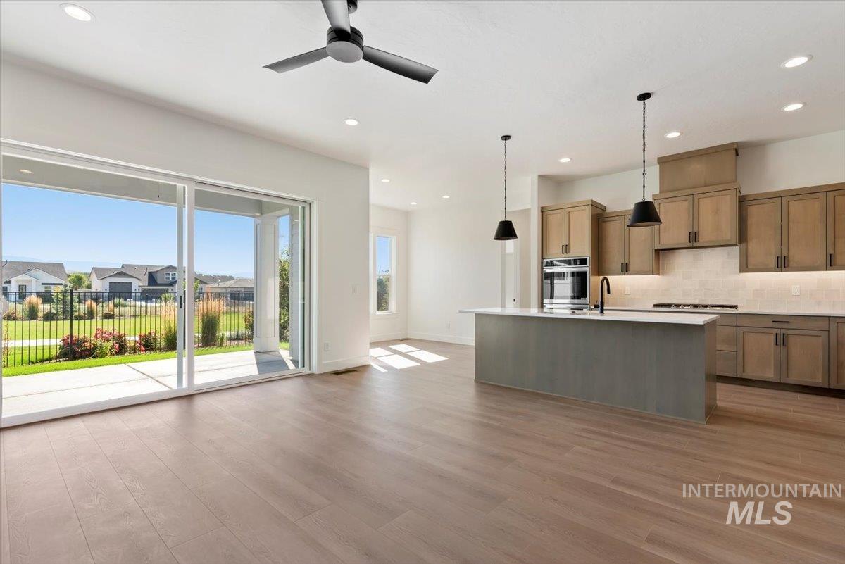 Kitchen with an island with sink, decorative light fixtures, decorative backsplash, light wood-type flooring, and recessed lighting